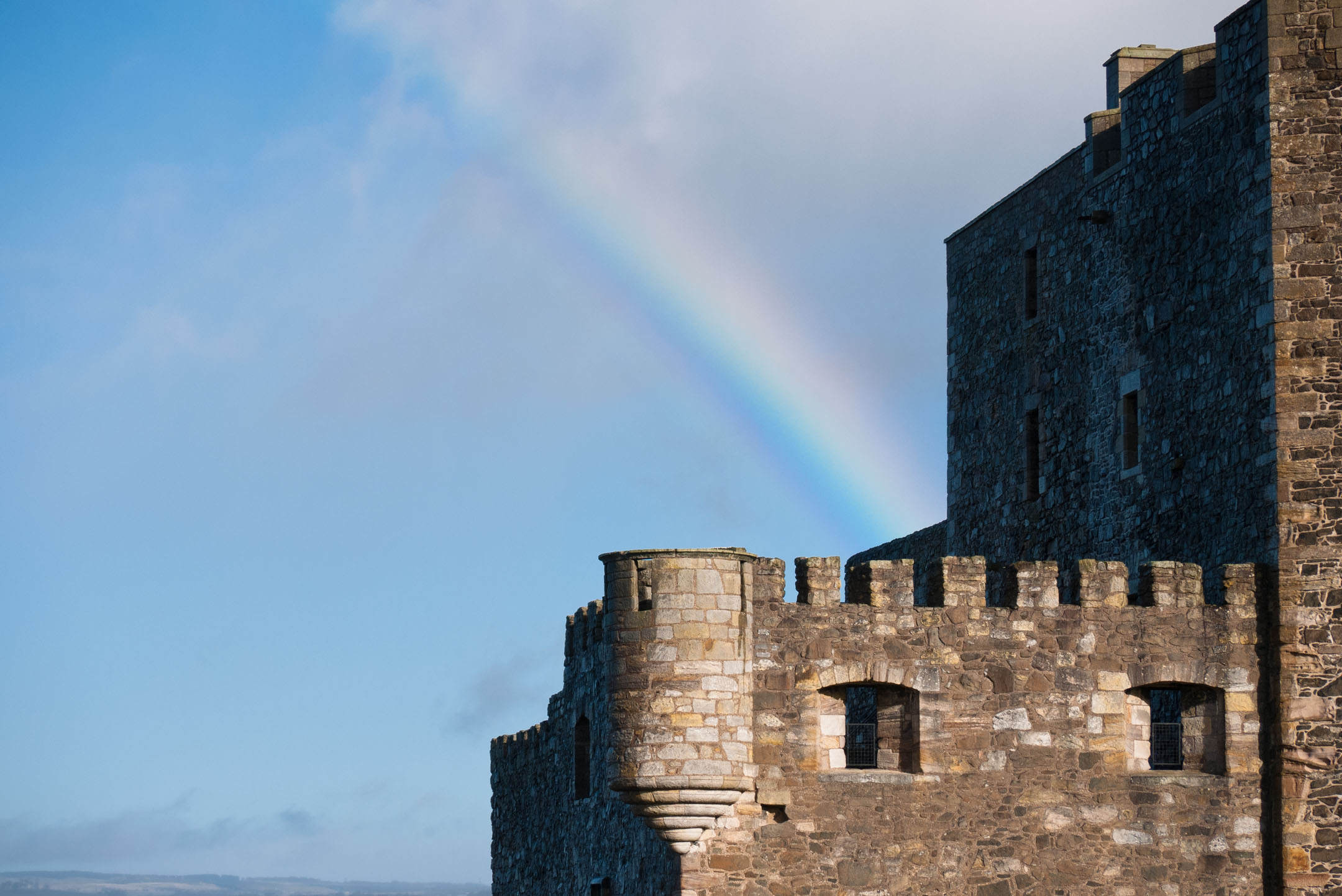 Close-up of castle wall with rainbow in bright blue sky.