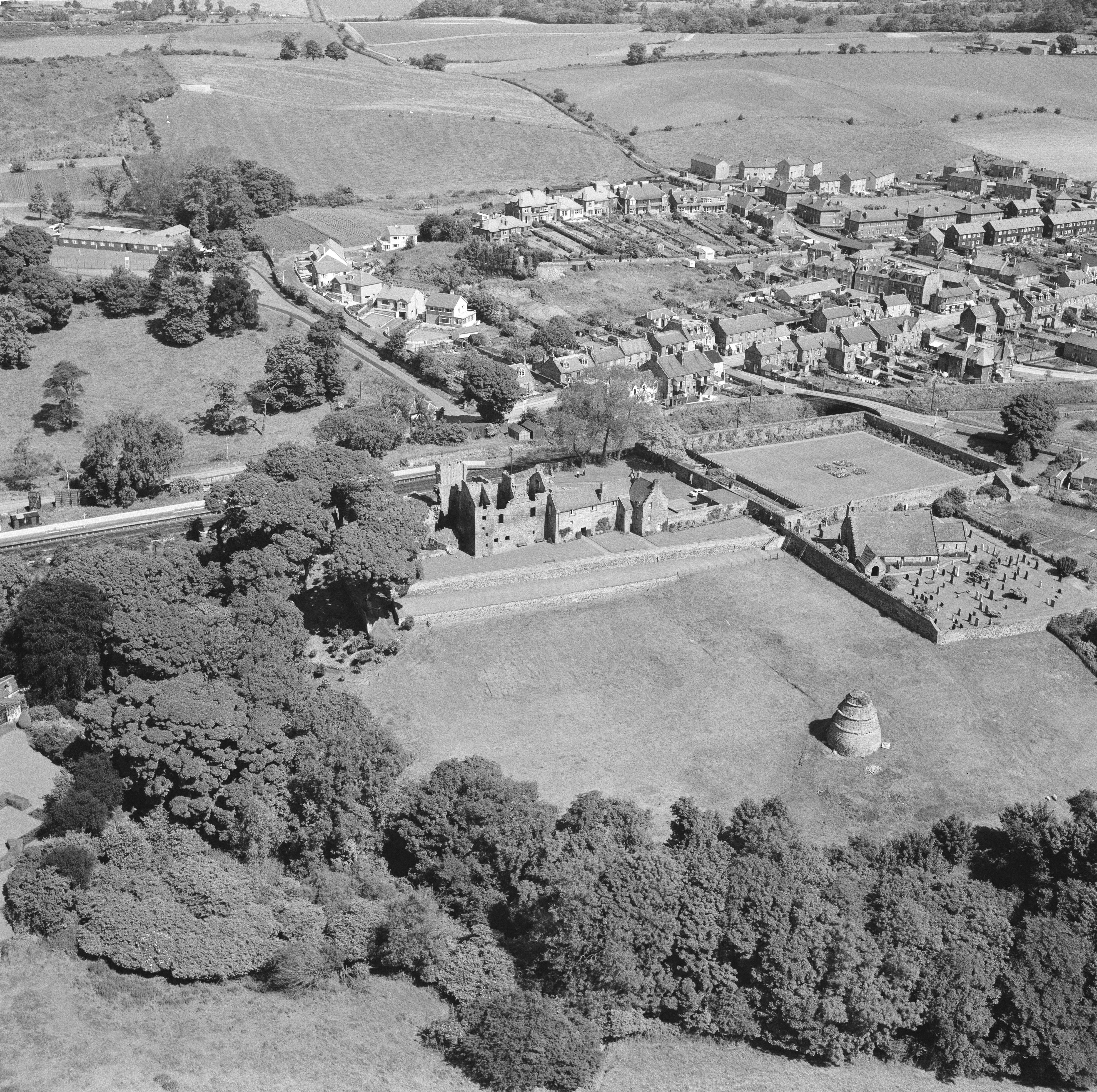 A large historic stone castle, with extensive grassy grounds and doocot, surrounded by trees and nearby to a housing estate