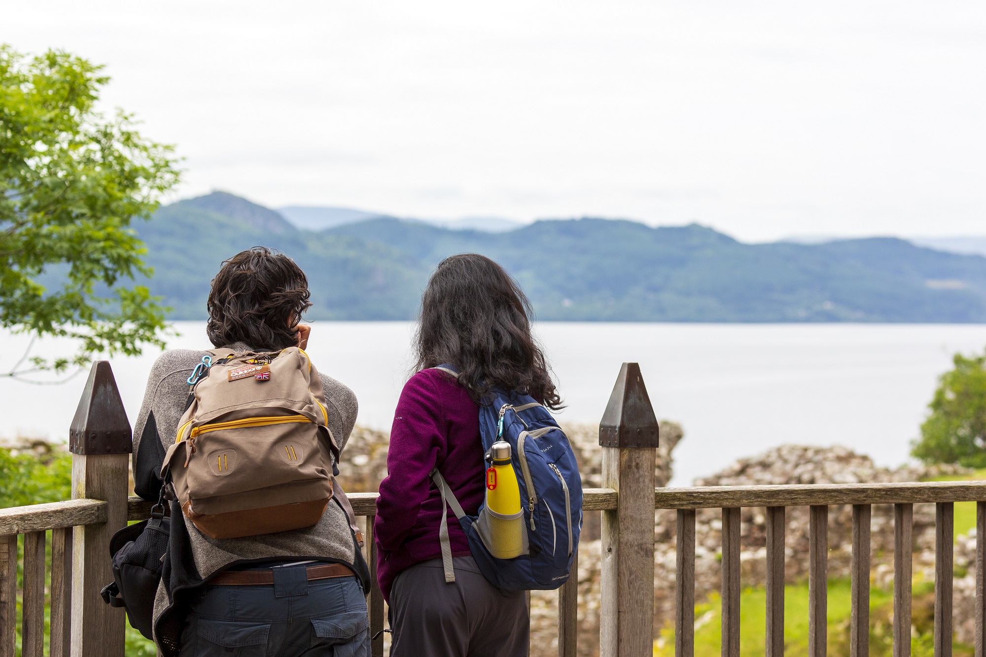 Two visitors to Urquhart Castle admire the view across the waters of Loch Ness to the trees and mountains beyond.