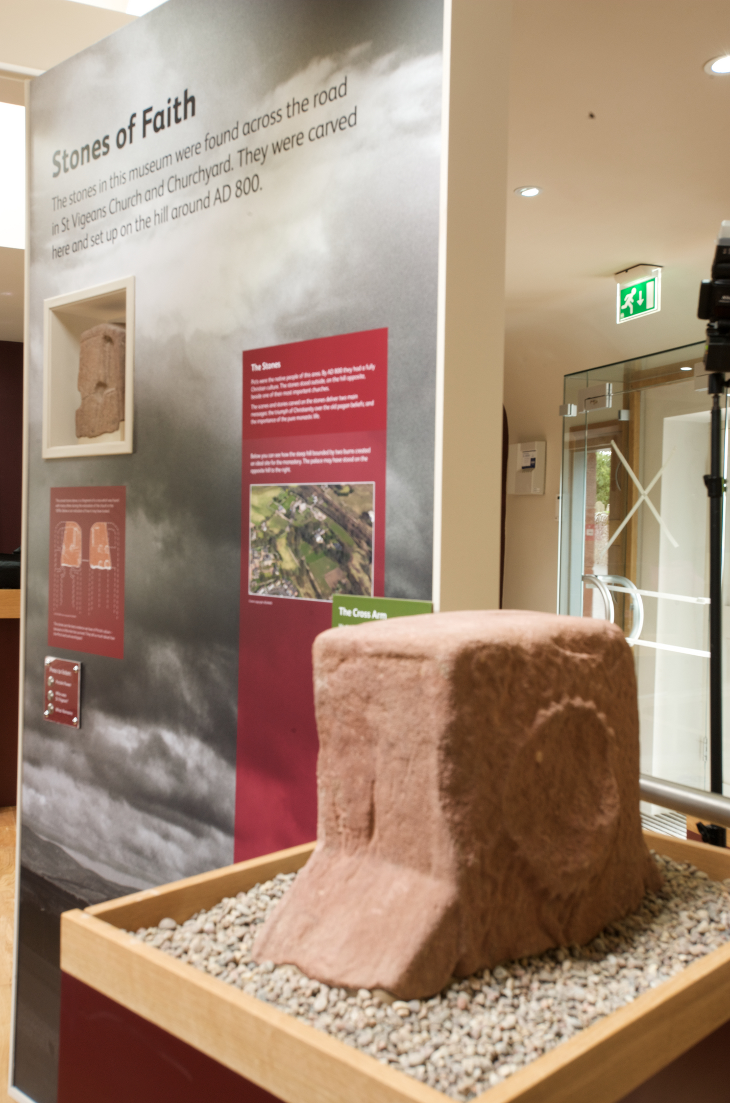 Museum panel titled “Stones of Faith,” showing interpretive text and photographs about Pictish stones. In front of the panel sits a carved sandstone block displayed in a tray of gravel.