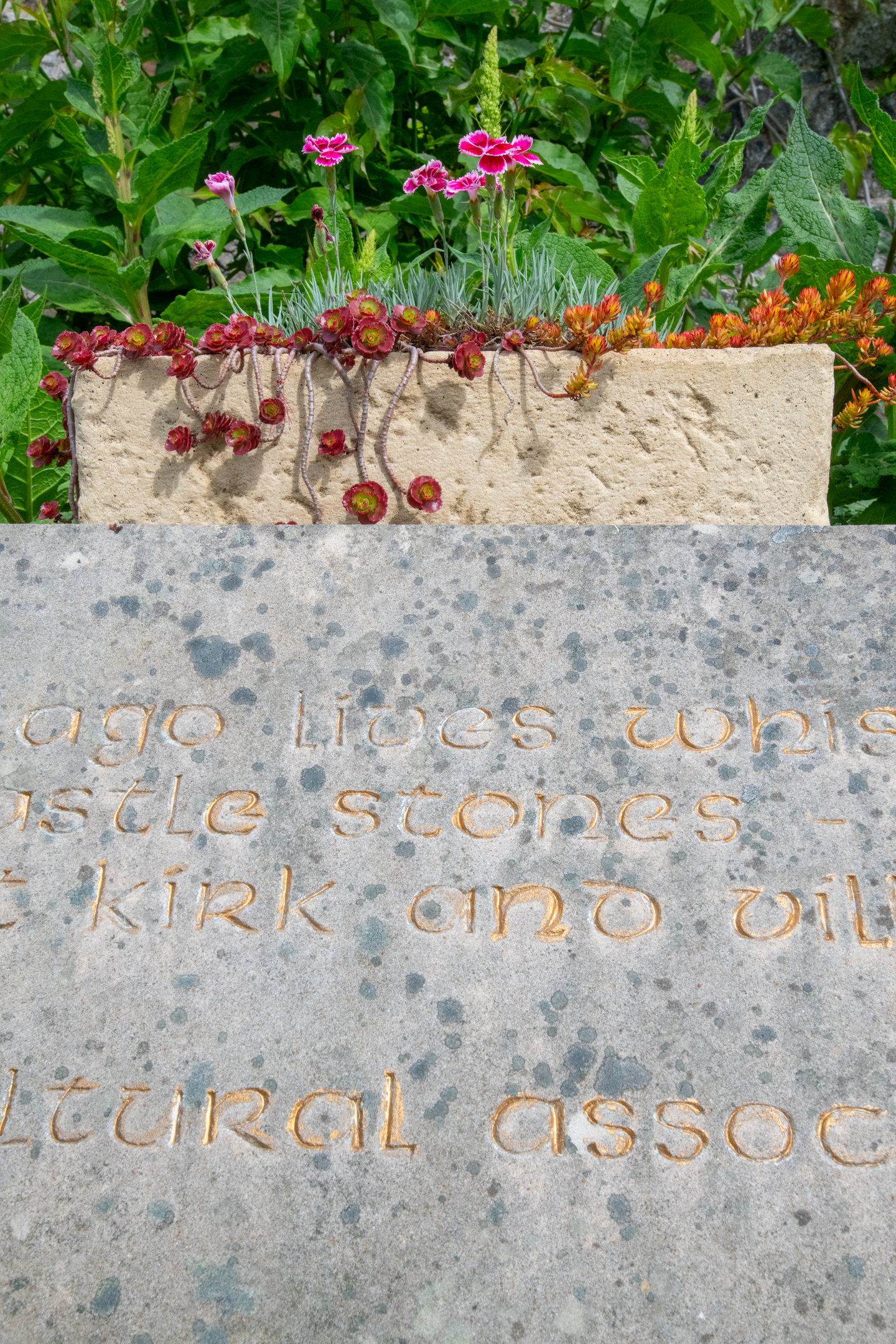A stone with words carved into it in gold and a stone planter sitting on top of it 