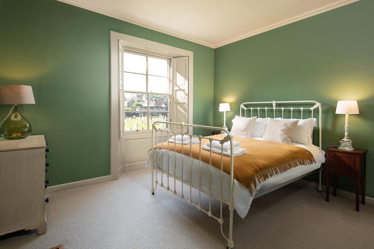A large green double bedroom, with a sash and case window and double bed with a yellow throw on it