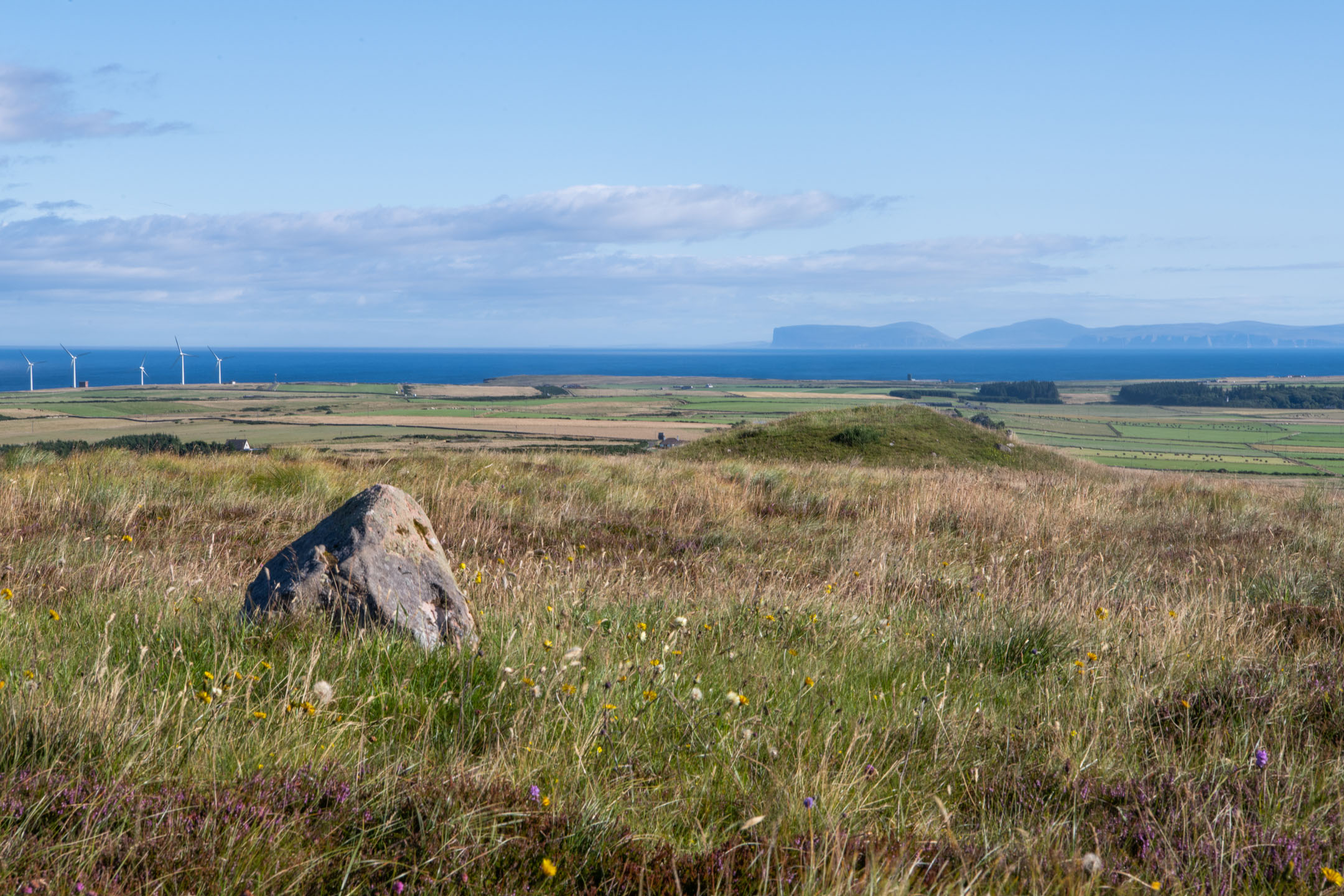 Single stone on grassy slope with distant sea and islands under clear sky.