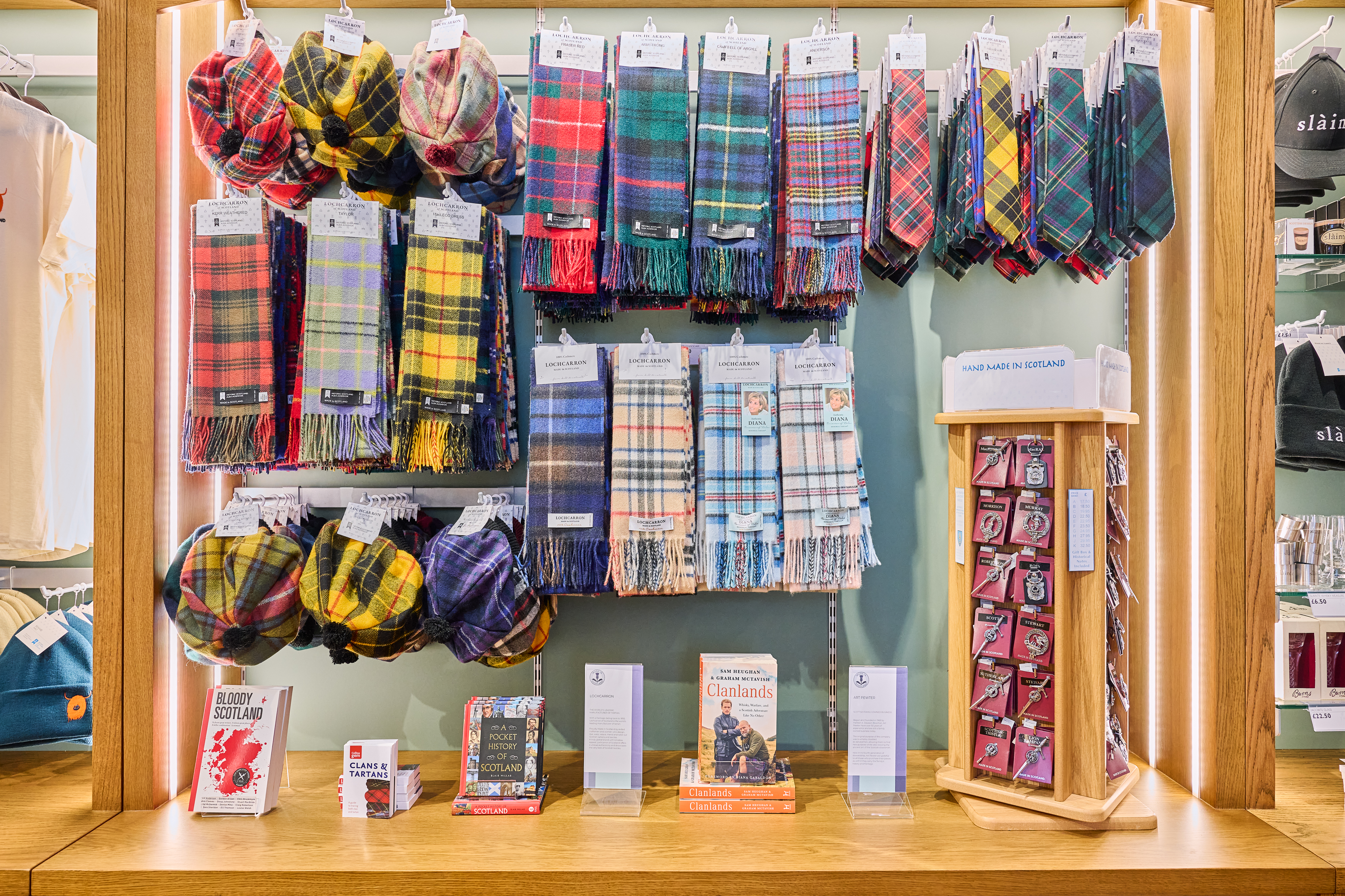 A well-organised wall display of tartan scarves in many colours and patterns, accompanied by small books and information stands.