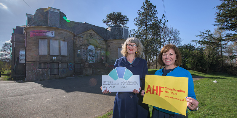 two women stand outside an old building smiling at the camera and holding up signs, one saying Historic Environment Scotland and the other AHF 