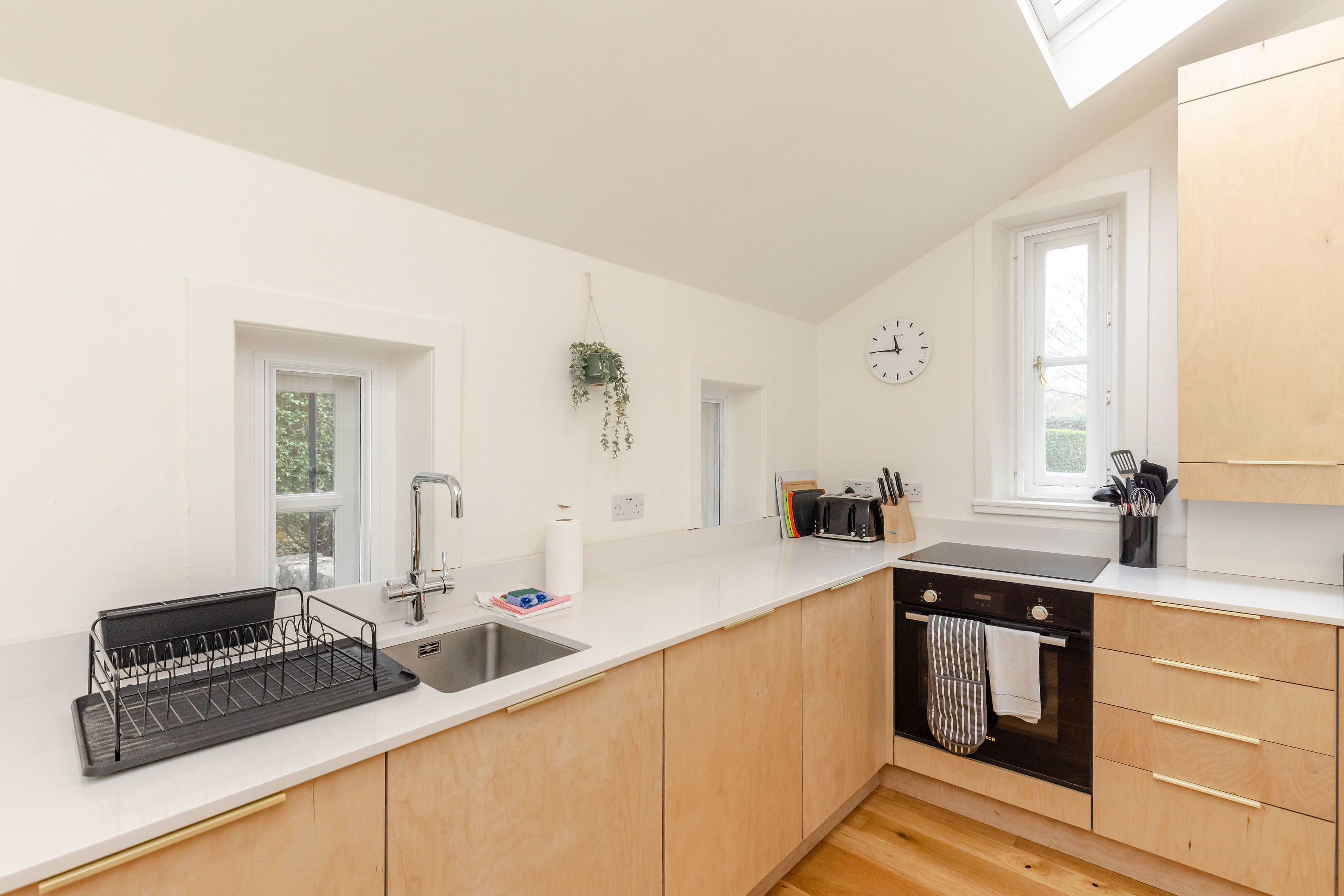 A clean and tidy kitchen with white white walls, wooden cupboard doors and drawers, and a white counter top