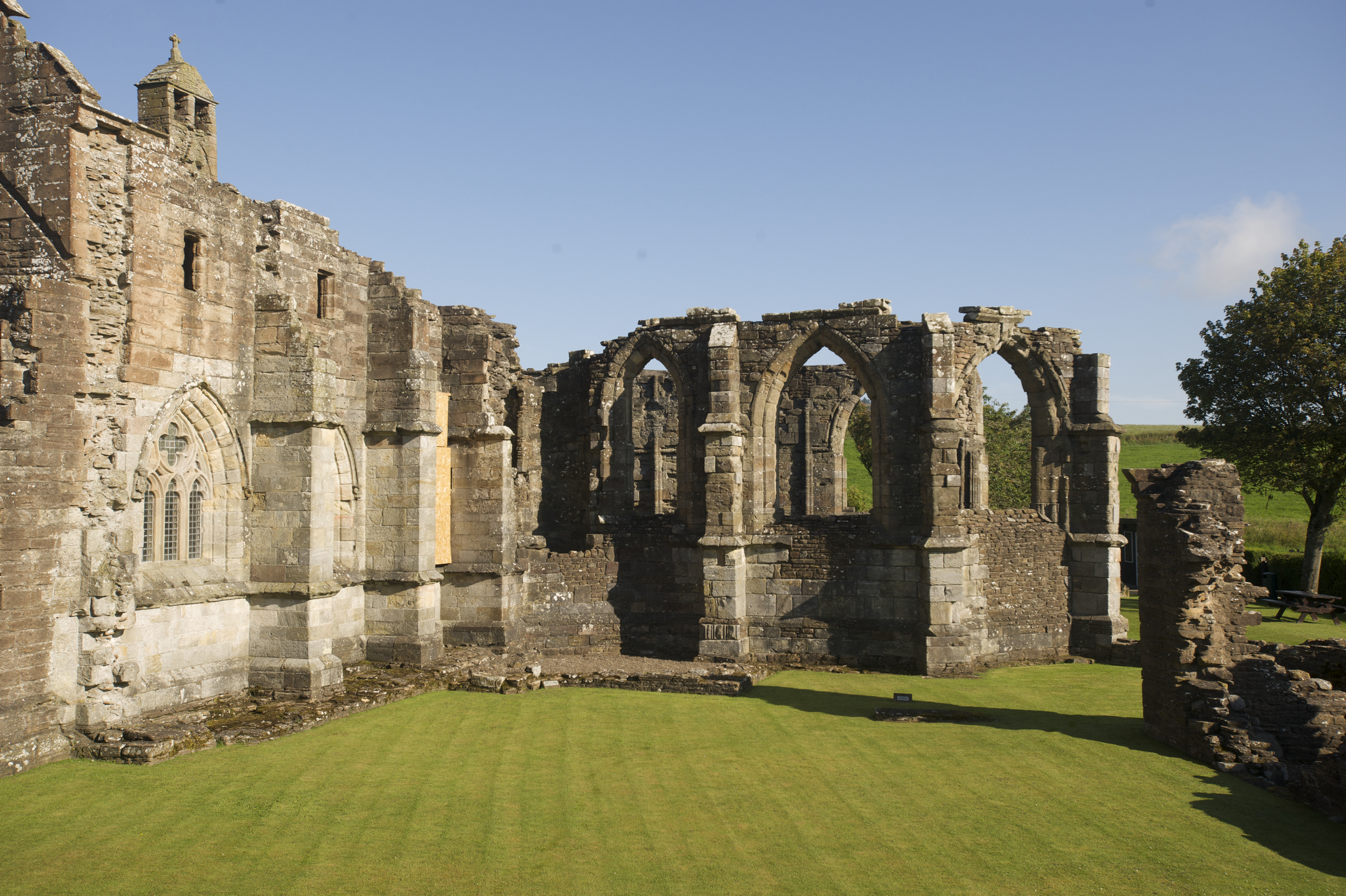 Section of Crossraguel Abbey showing tall Gothic arches and stone walls bordering a well-kept green lawn.