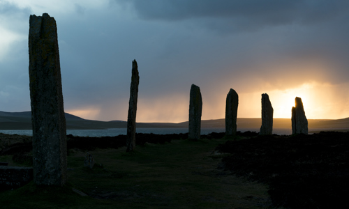 The ancient standing stones at the Ring of Brodgar are silhouetted by a sunset