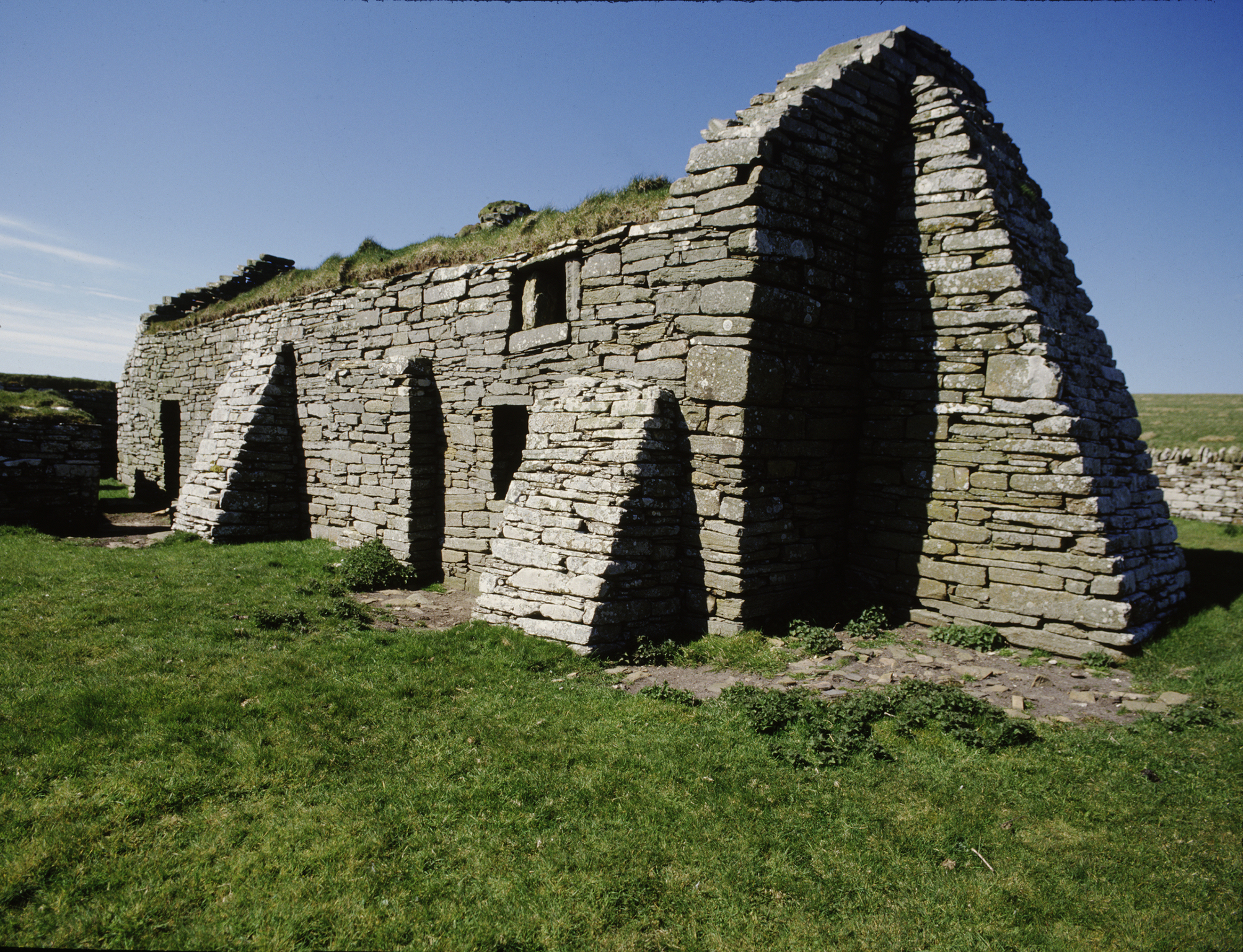 stone ruins of a long rectangular building with triangular buttresses and a turf roof