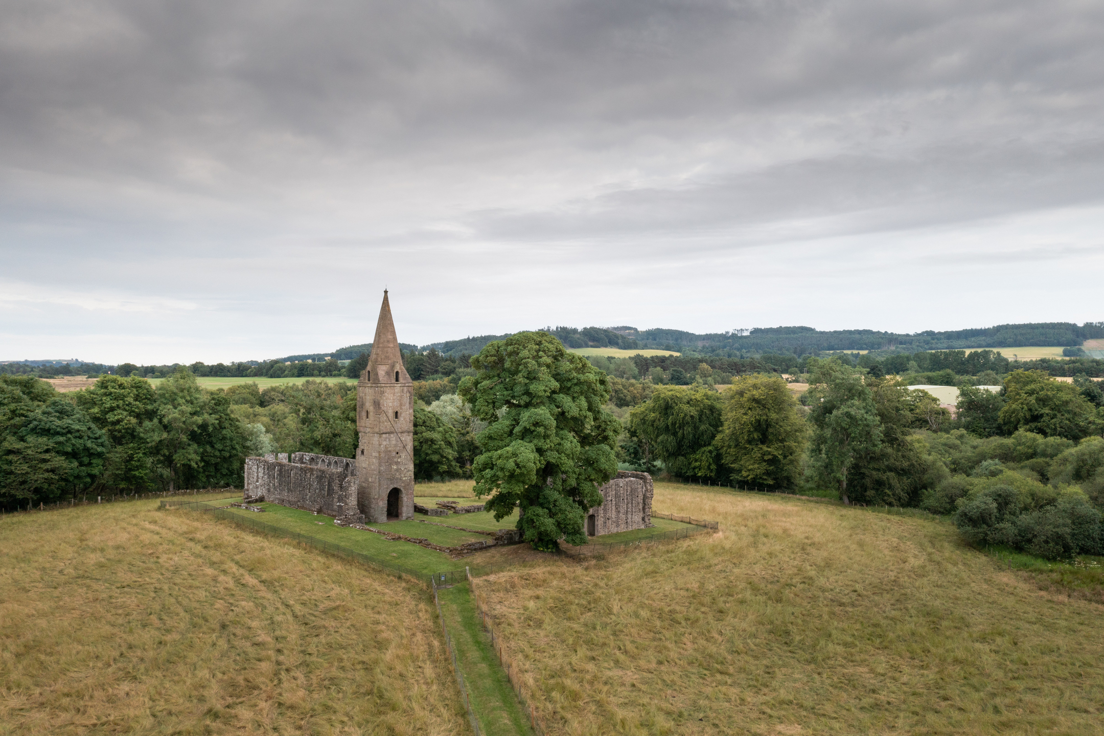 Grey clouds, parched grass, green trees and what remains of a priory, including a well-preserved tower
