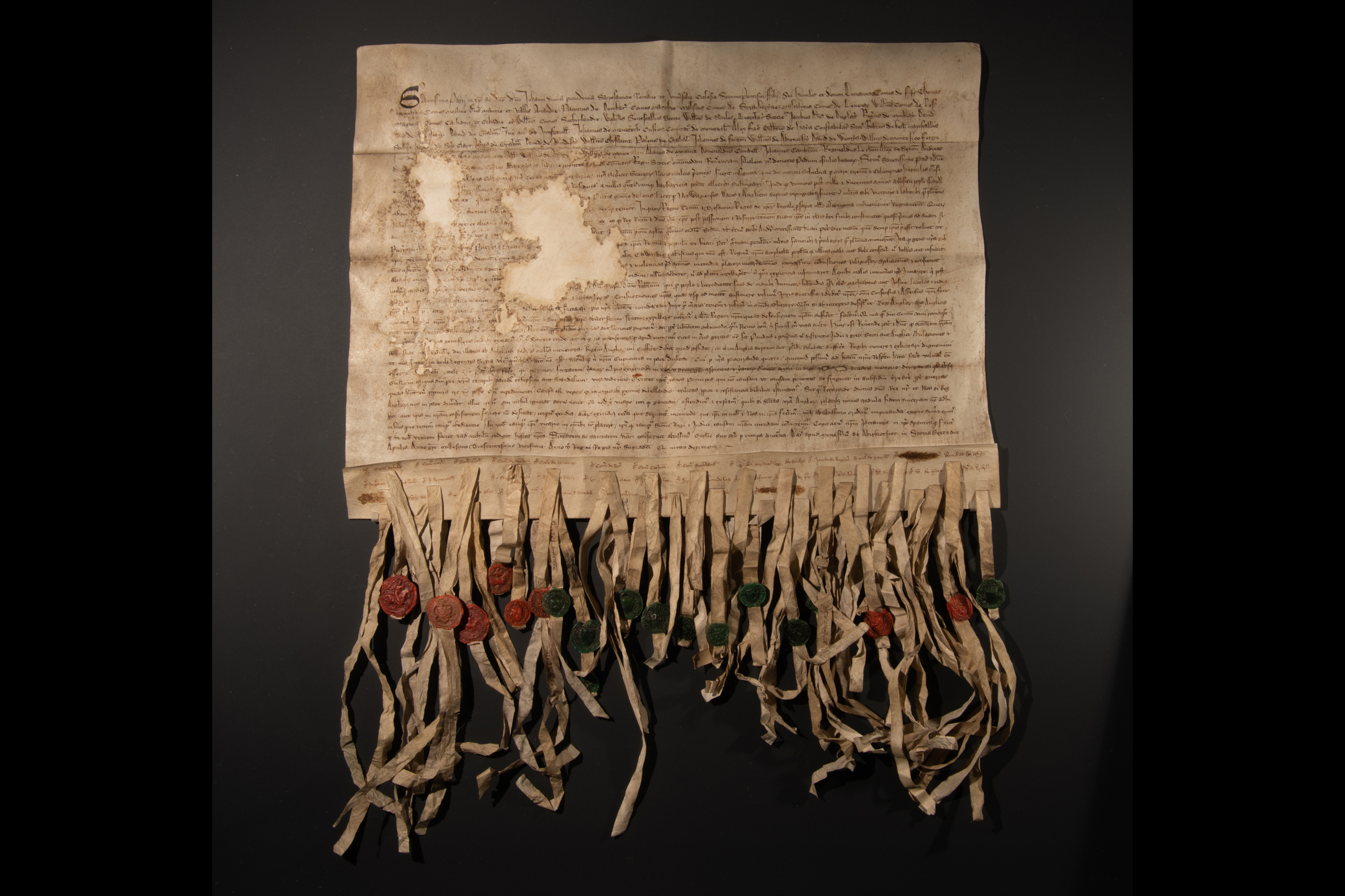 Discoloured paper with detailed text and strips at the bottom that have red and green wax seals attached