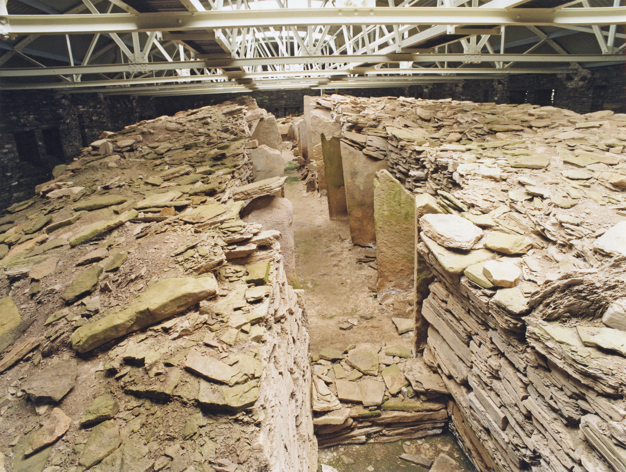 Wide interior landscape view of the cairn showing stacked stone walls, upright partitions, and the protective roof structure overhead.