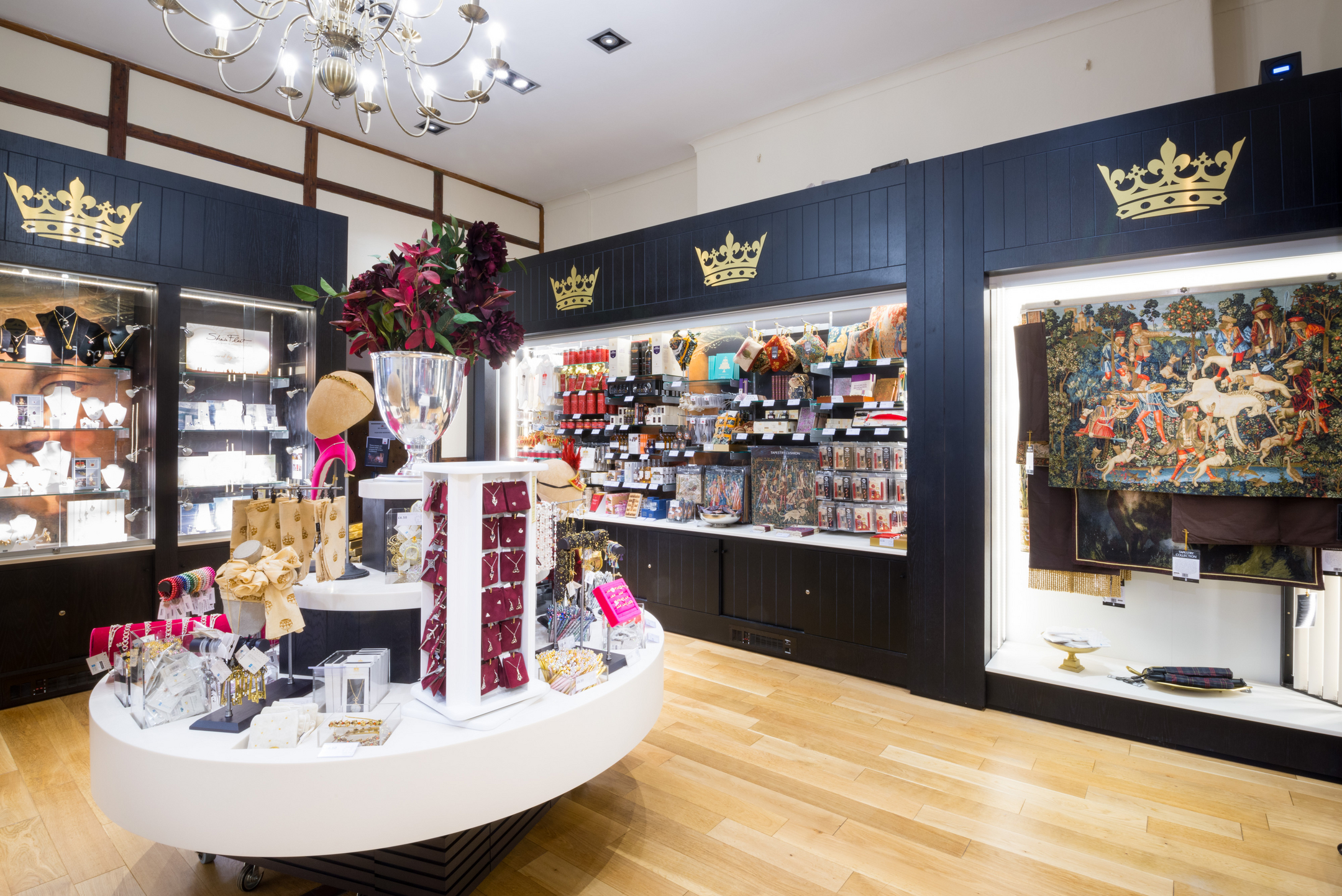 Interior of a gift shop with crown motifs above displays of jewellery, textiles, and souvenirs arranged on dark shelving.