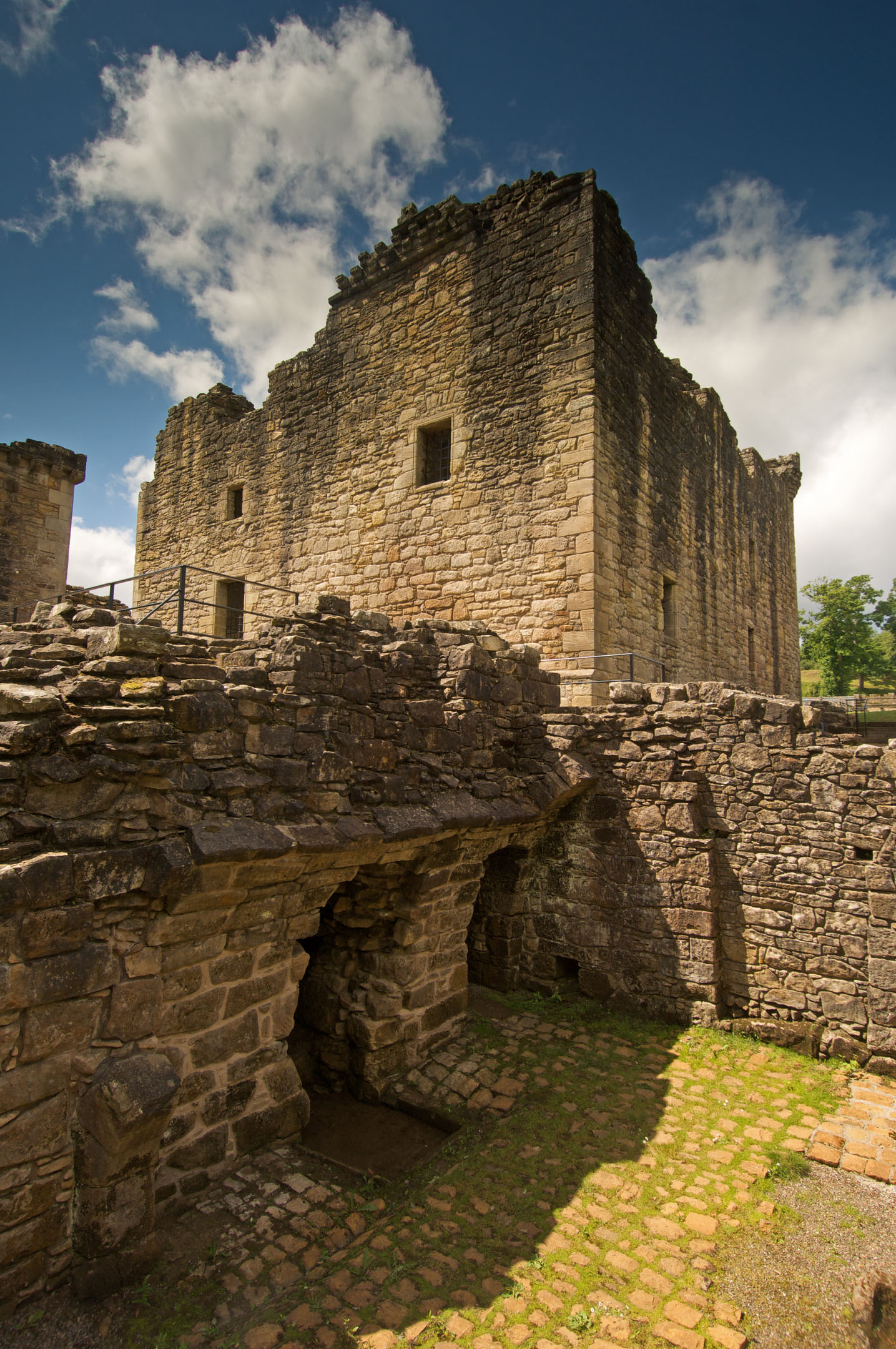 Castle ruins with stone forecourt and green grass under bright sky.