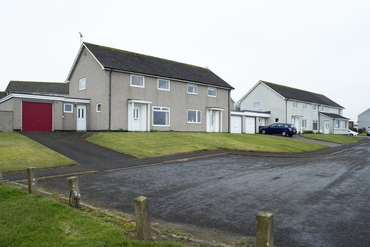 Grey house with attached garage under a grey sky with grass and tarmac outside it.