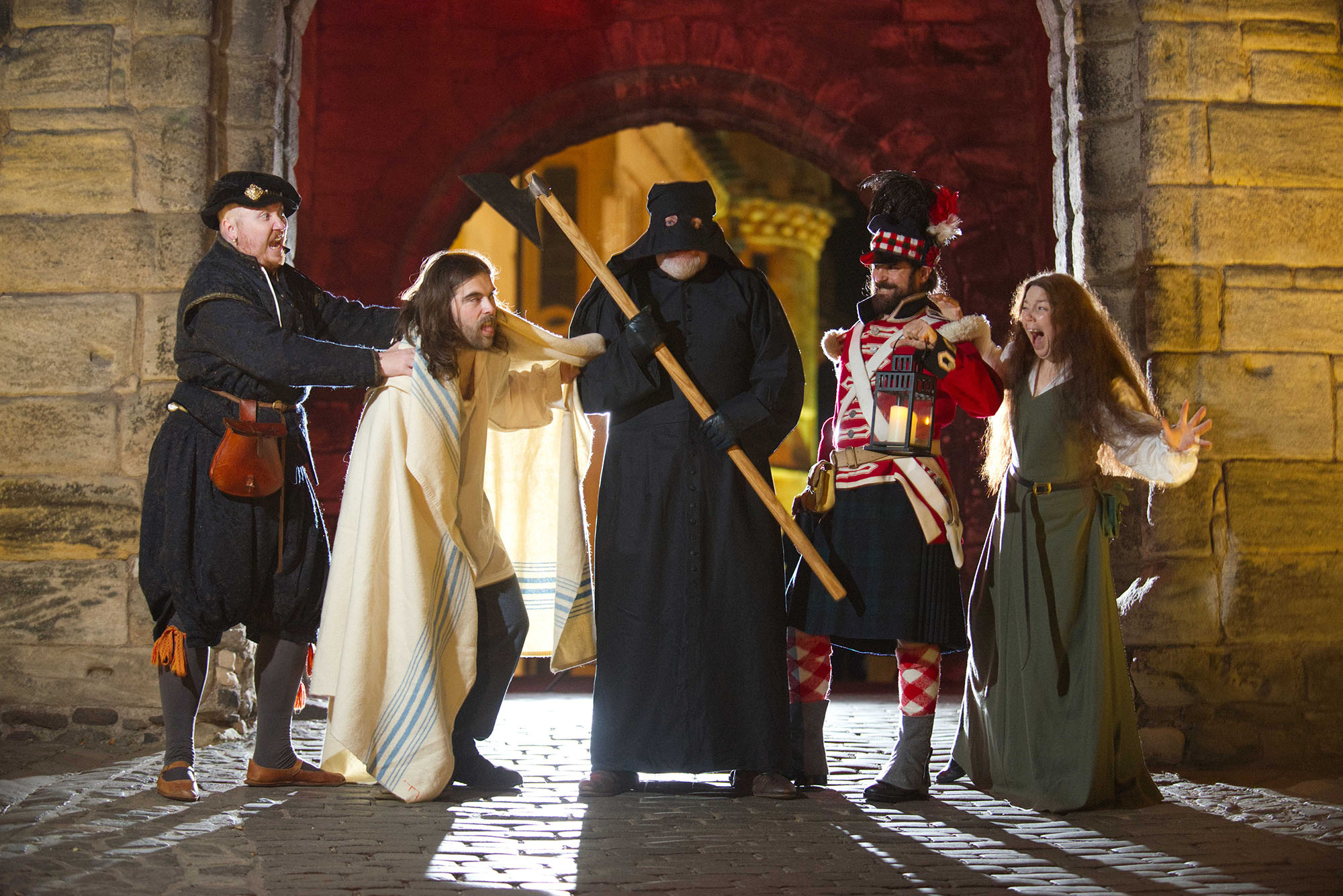 Five costumed performers dressed as characters from different time periods stand in a line in Stirling Castle with a partial view of the Royal Palace behind them