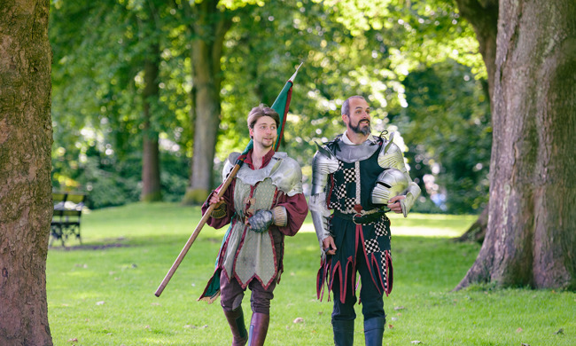 Two performers dressed as knights take a walk in a park