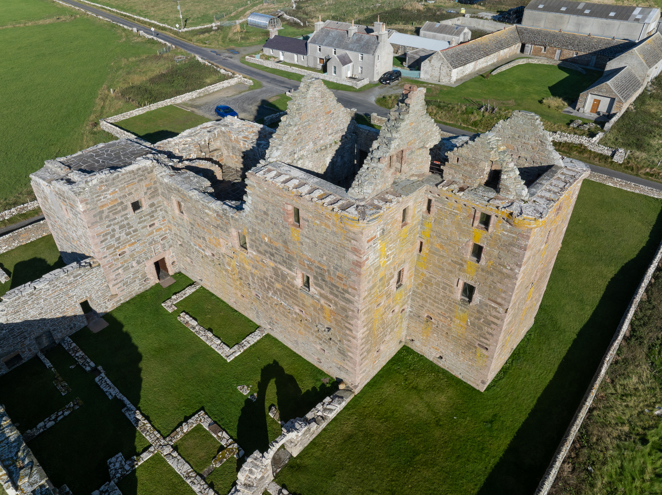 Aerial view of Noltland Castle’s layout, including roofless stone halls, grass-filled courtyards, and the surrounding boundary walls.