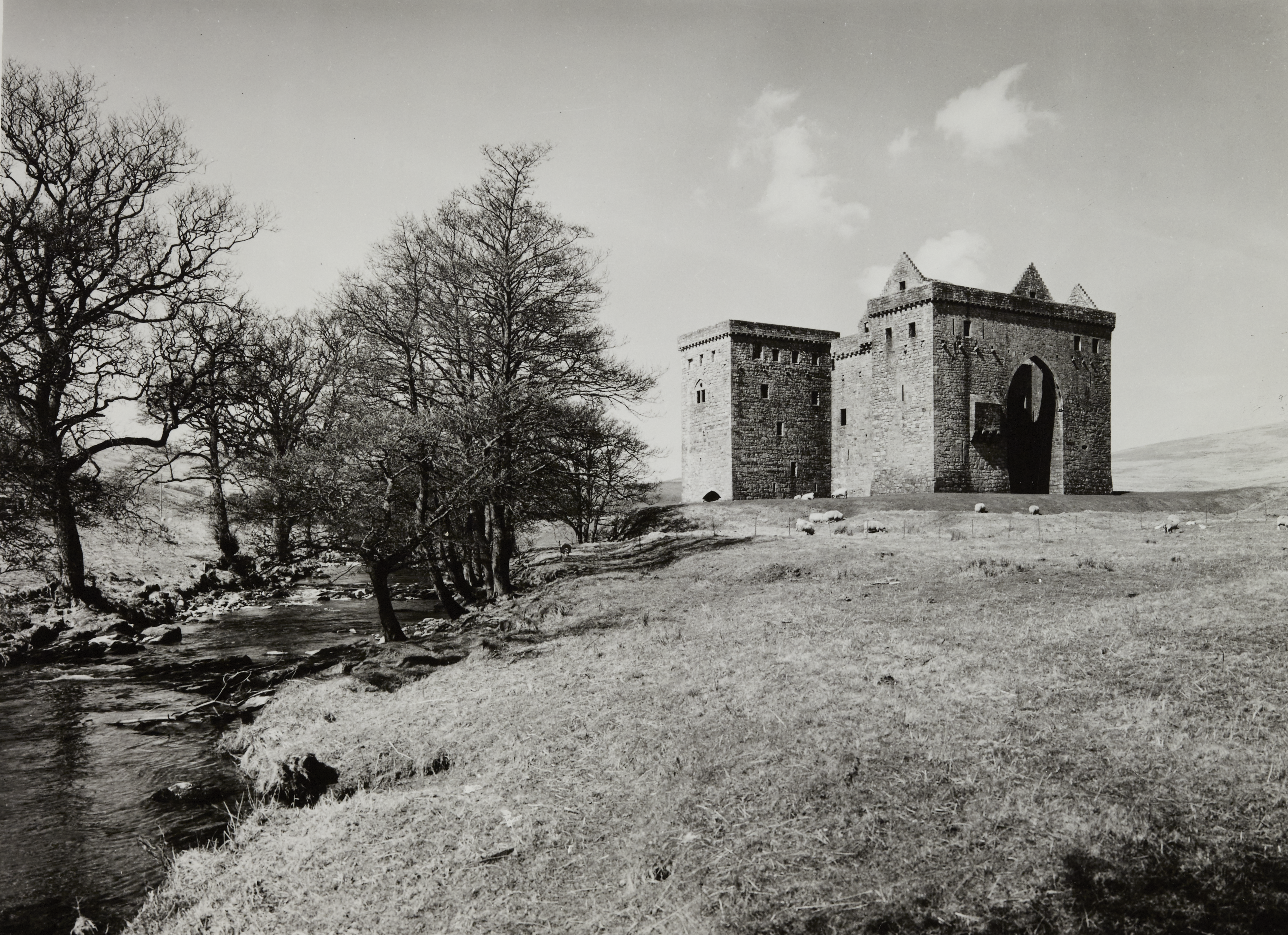 Black and white photo of castle by a small river with trees