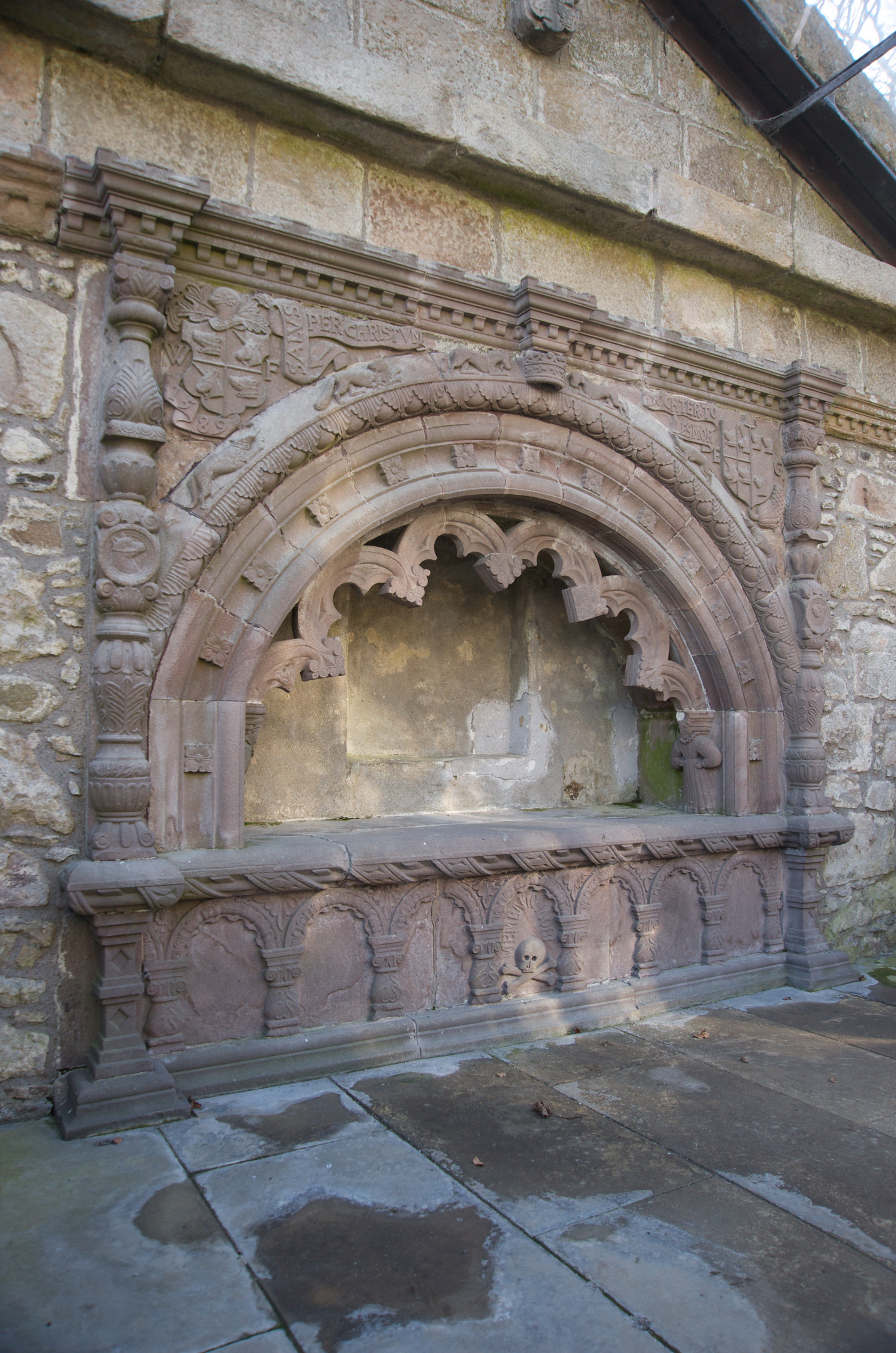 An ornately carved stone tomb featuring an archway over a recessed shelf space. 