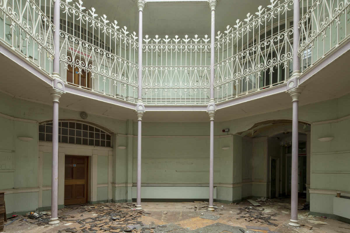 Octagonal hall area with thin columns and decorative railings at upper floor, with debris on lower floor