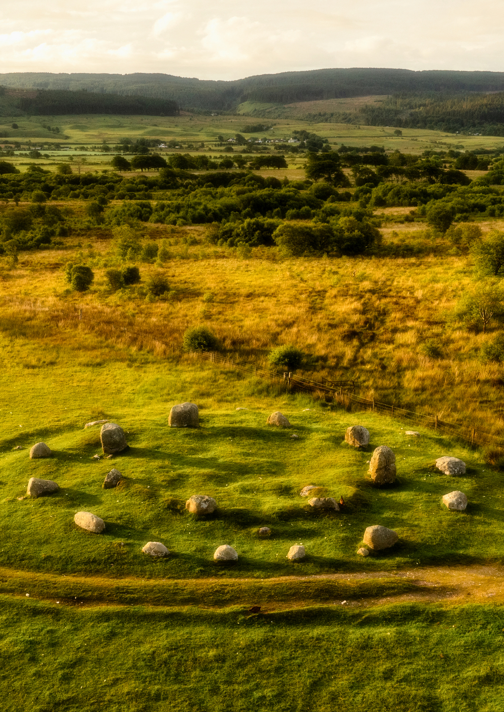 Stone circles on a rural landscape, with trees and hills in the background. 