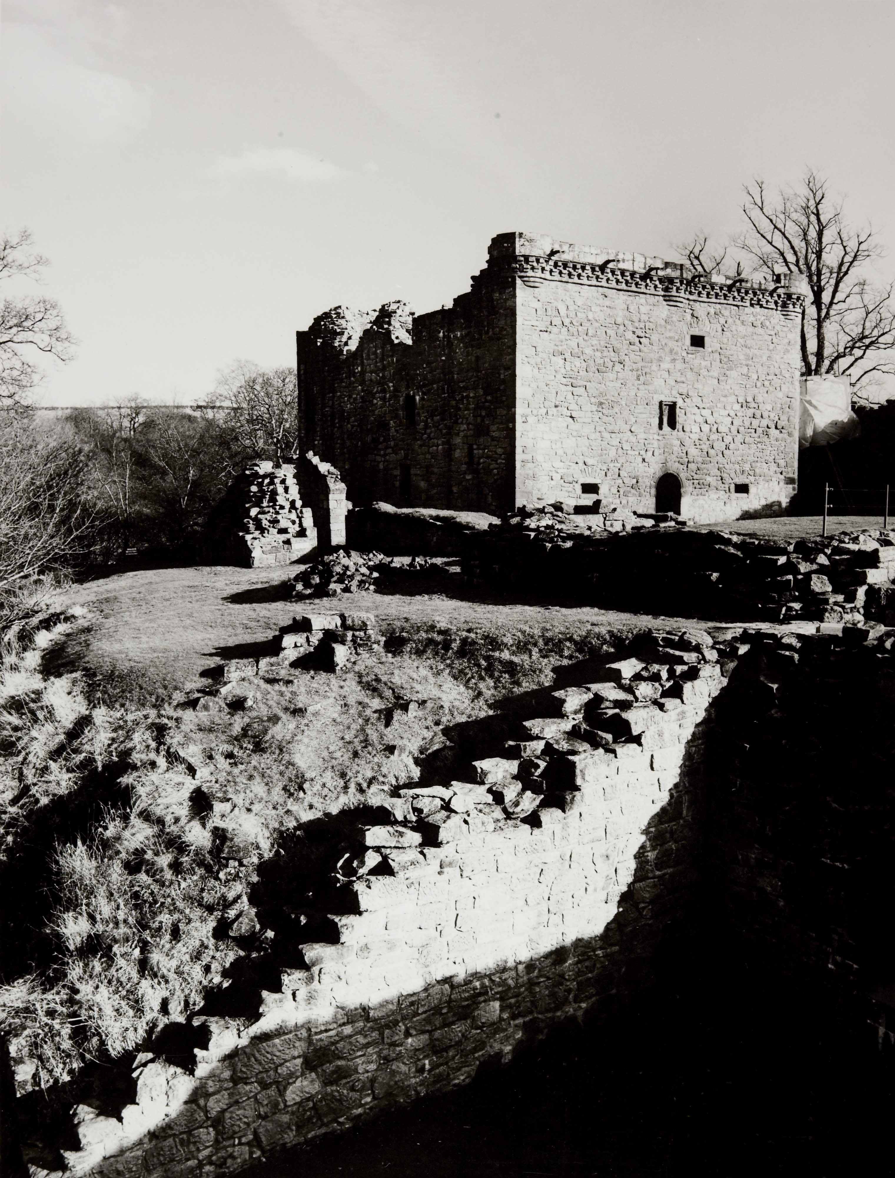 A rectangular stone castle, with partially ruined walls surrounding it