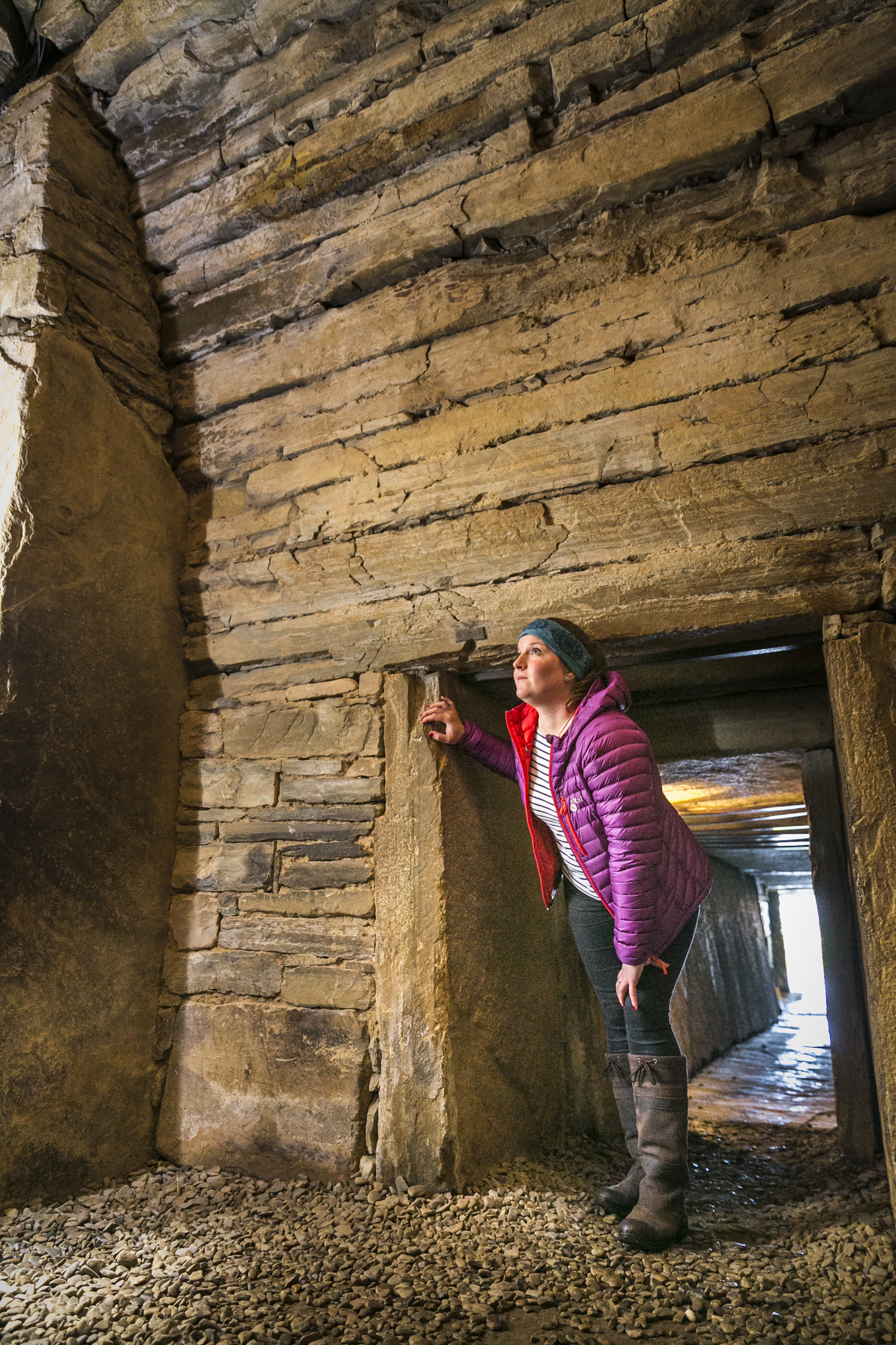 Women stood in the entrance of a neolithic burial chamber made of stone, peering inwards