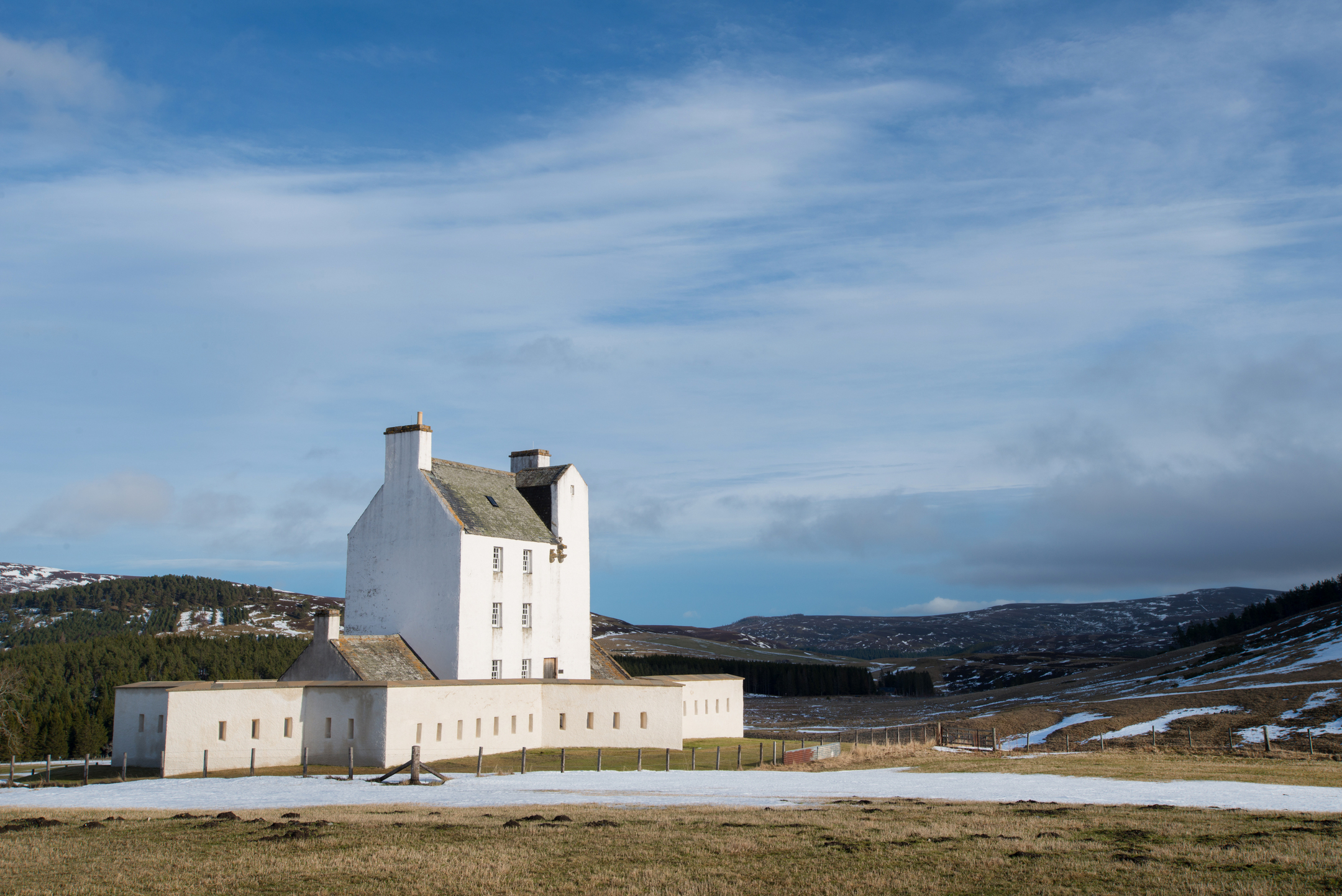 Side view of Corgarff Castle with its white tower and star-shaped perimeter wall, surrounded by snowy ground and open hills.