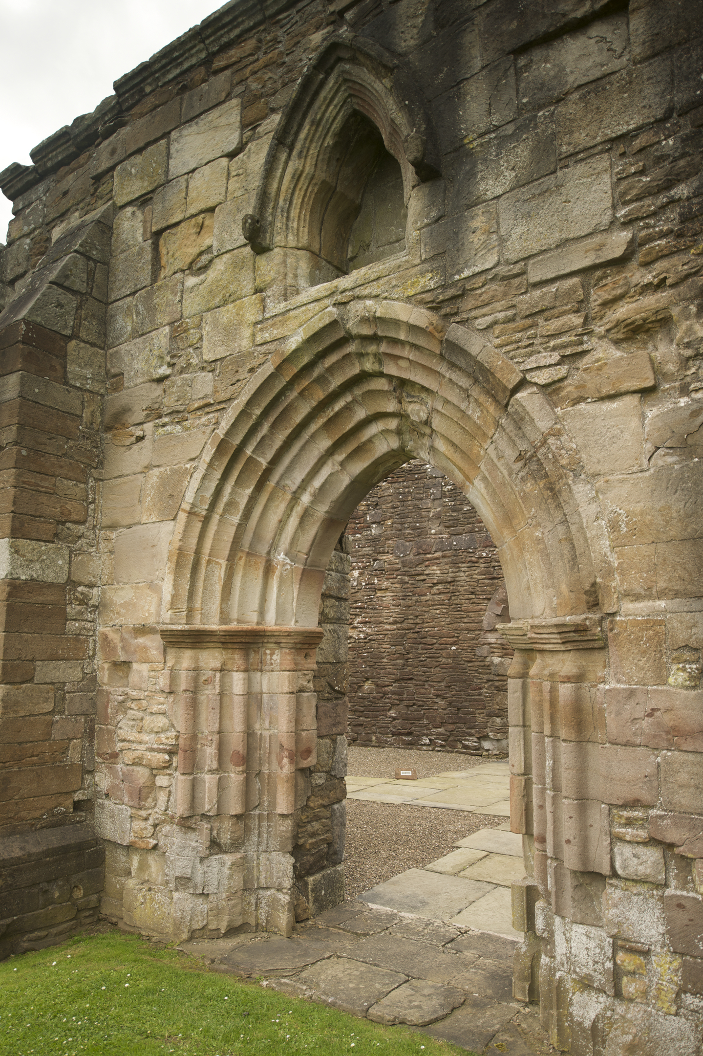 Stone archway with layered Gothic-style moulding at Crossraguel Abbey, showing weathered blocks and an opening into the inner ruins.