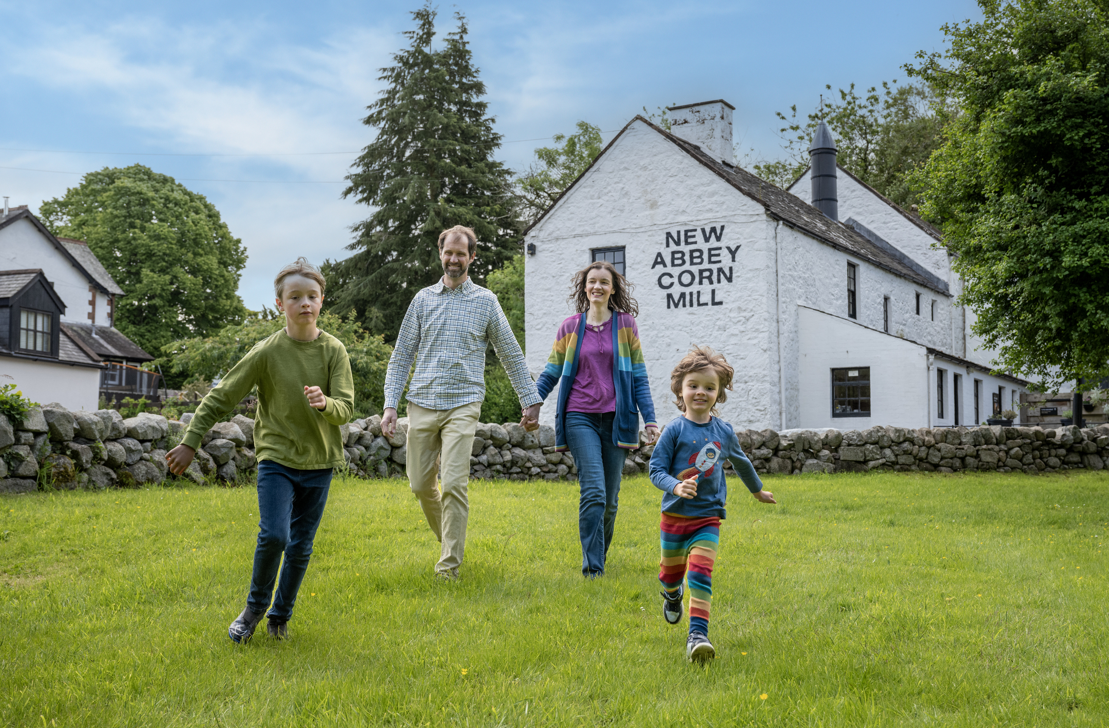 A family walking across a grassy lawn with the New Abbey Corn Mill building in the background.
