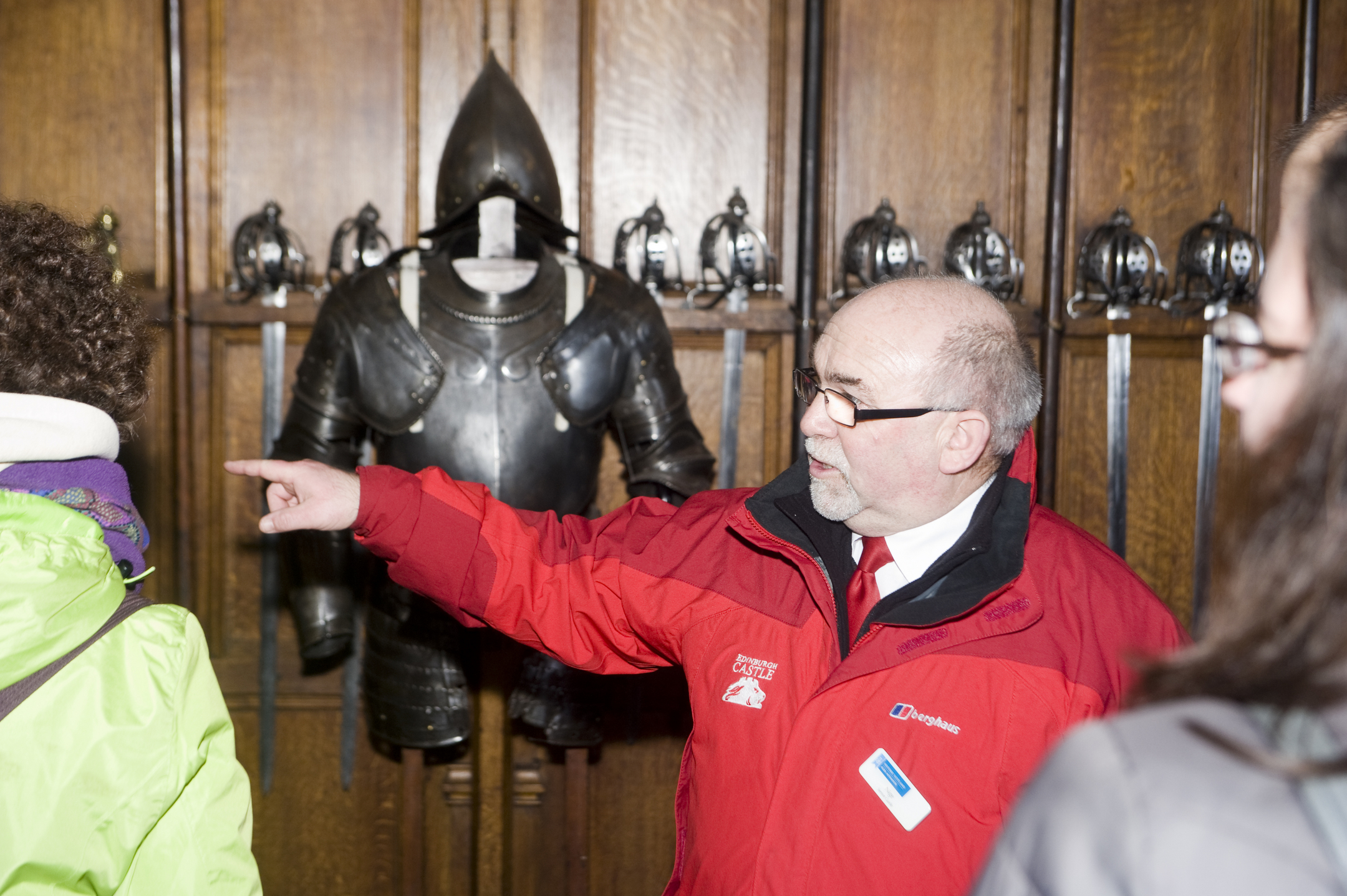 A castle tour guide points out something of interest to visitors. He is flanked by a suit of armour! 