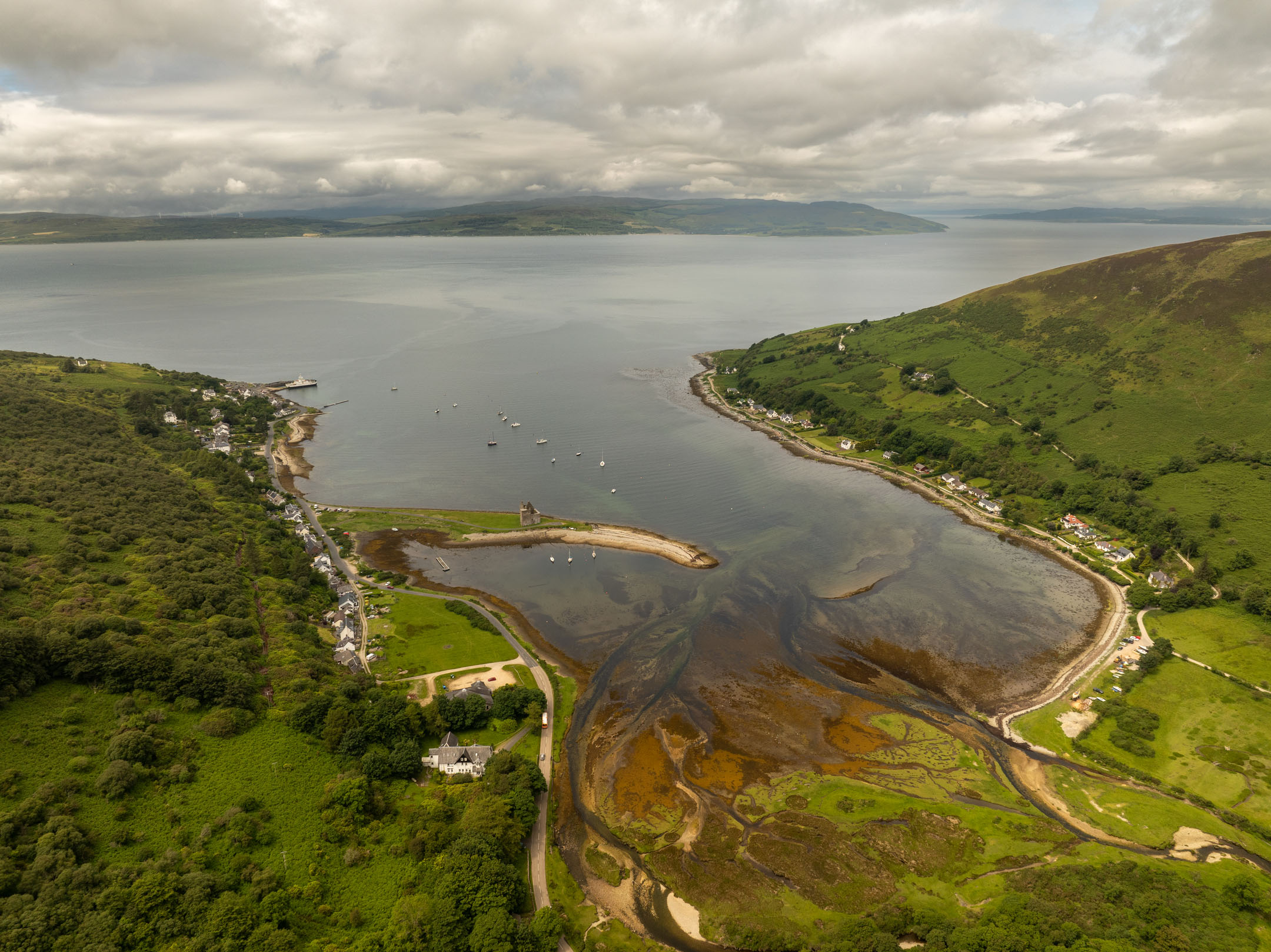 Broad aerial view of bay with castle on peninsula and surrounding hills.