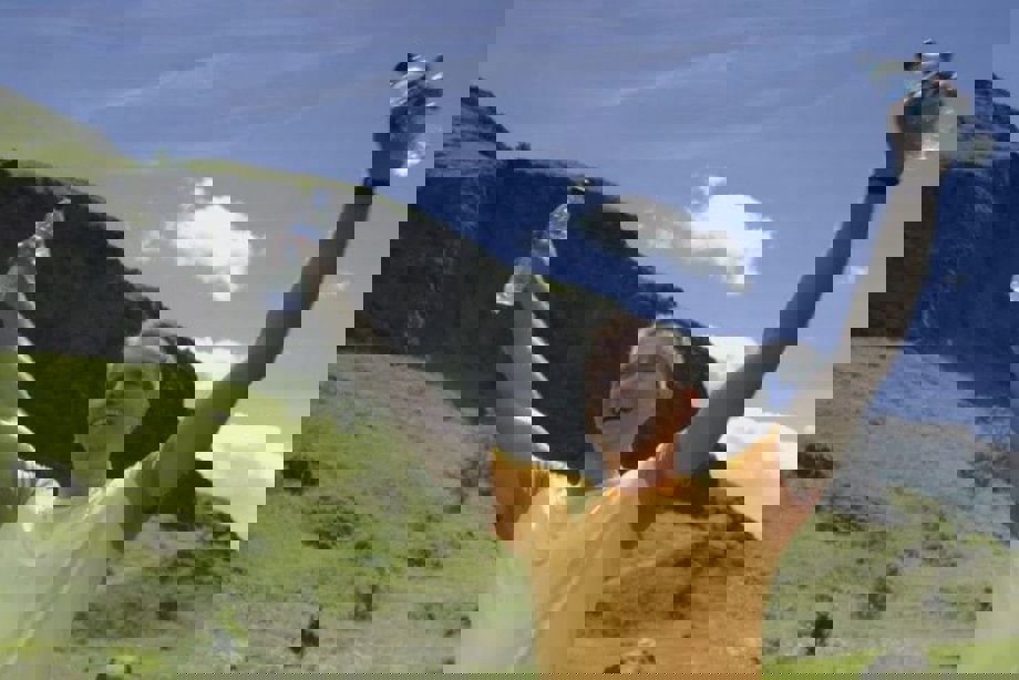 A man in a yellow tshirt on a grassy hill holding a bottle of water in each hand up above his head