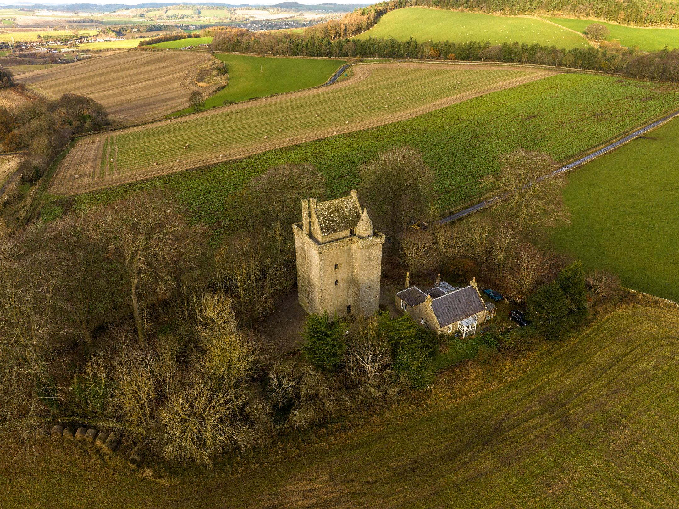 An aerial photo of a stone tower house surrounded by wintry trees and a mixture of pastural and arable farmland.