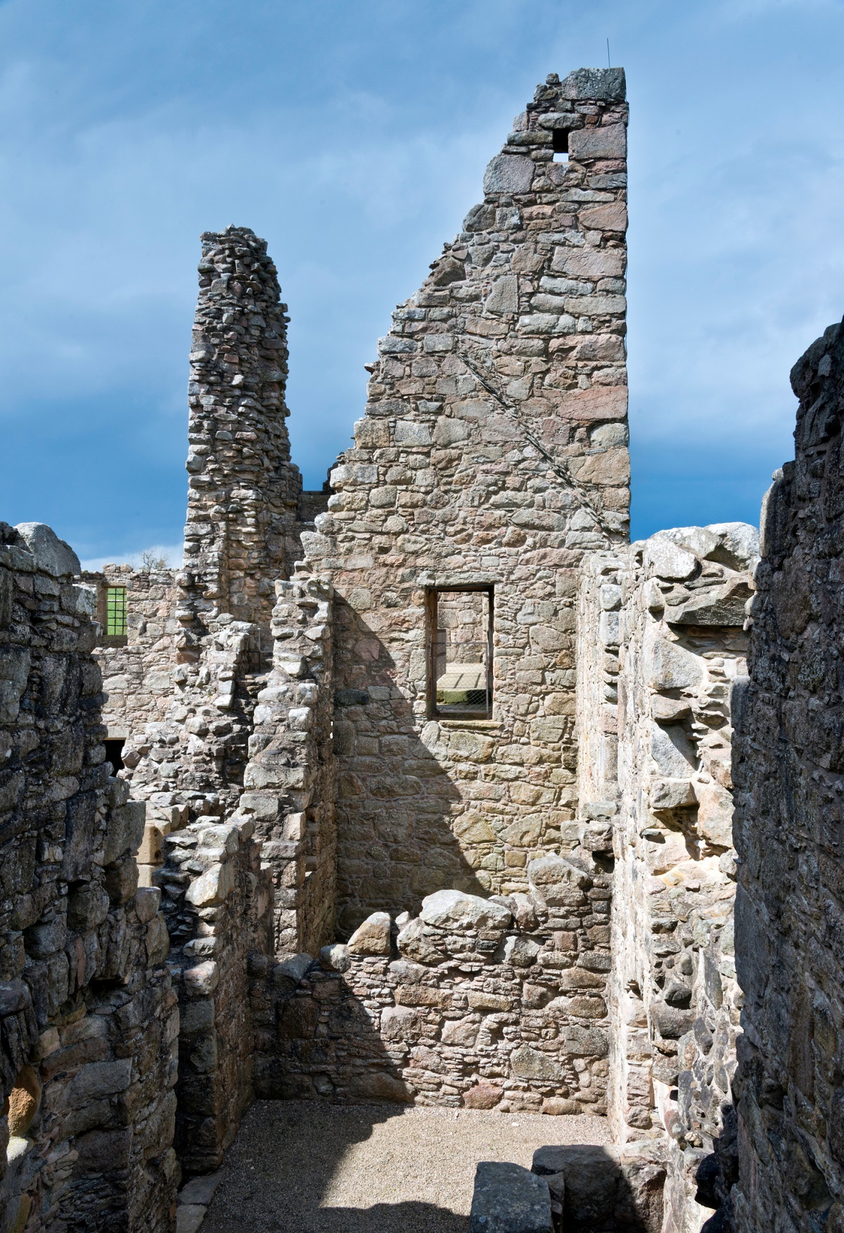 Interior ruins of Tolquhon Castle, with tall, jagged stone walls and an open window frame against a lightly clouded sky.