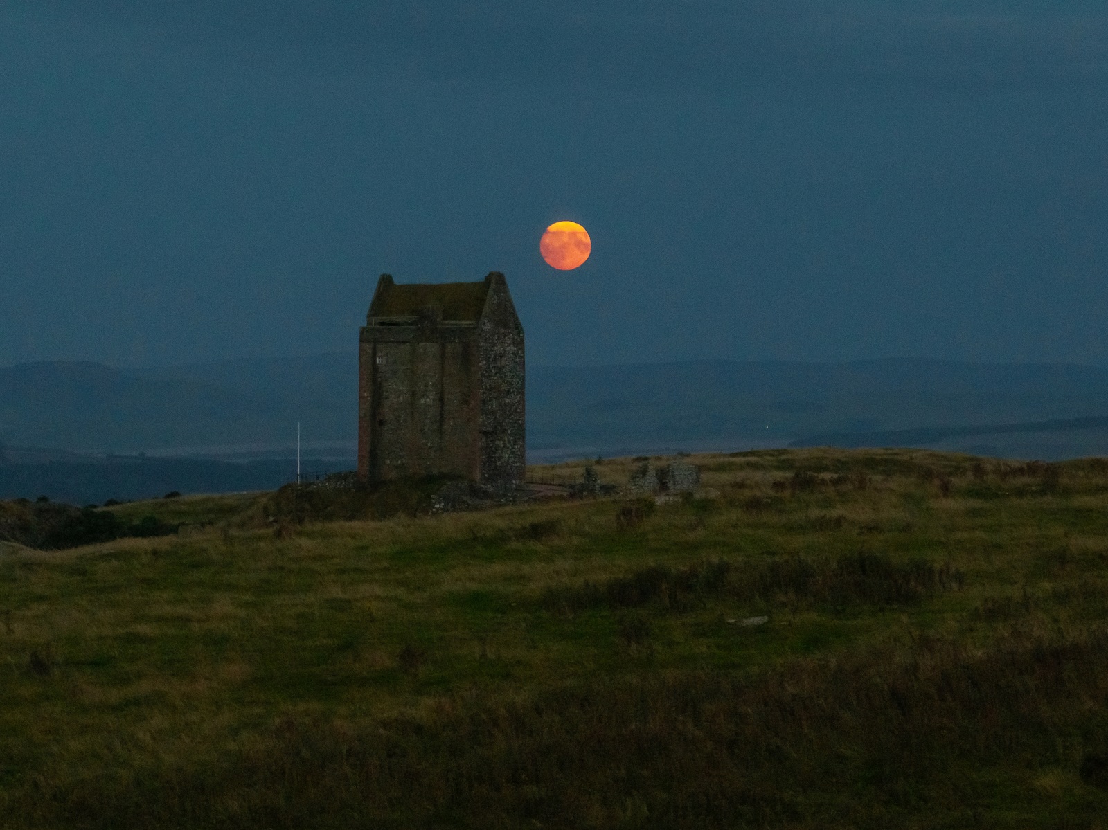 Stone tower at dusk with a large orange moon rising behind it.