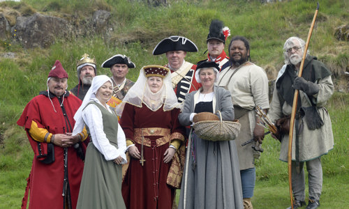 A group of costumed performers posing for a picture on a grassy hill