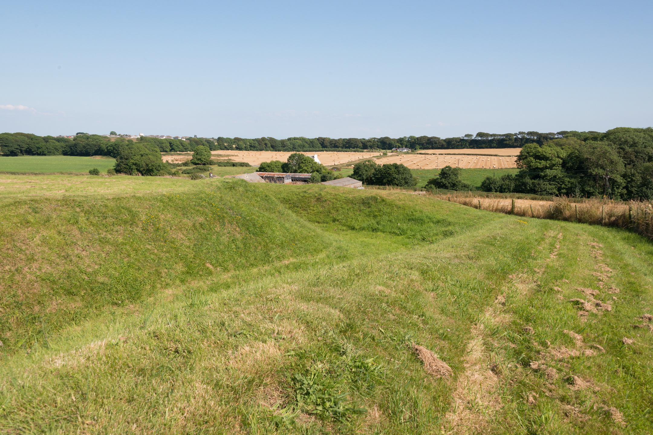 A view across grass-covered Iron Age earthworks to a farm and fields beyond