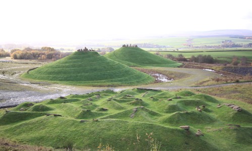 Crawick Multiverse - green landscaped mounds to foreground and background, hills and white sky behind