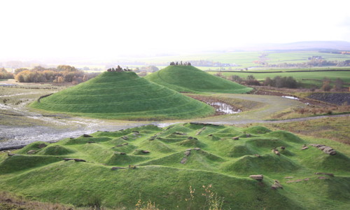 Crawick Multiverse - green landscaped mounds to foreground and background, hills and white sky behind