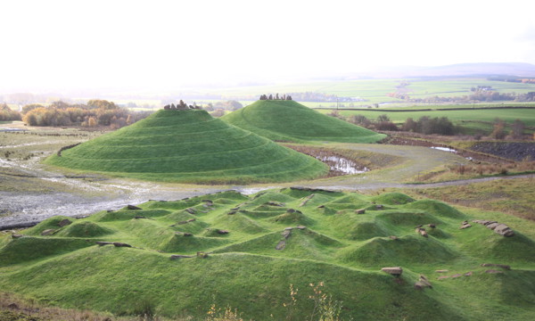 Crawick Multiverse - green landscaped mounds to foreground and background, hills and white sky behind