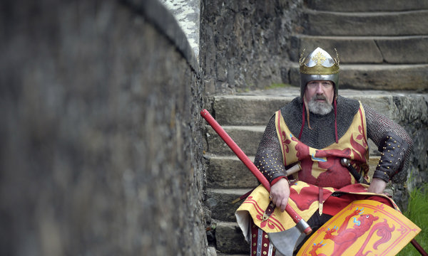 A costumed performer in chain mail with helmet and shield, looking stern sitting on concrete stairs