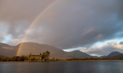 A rainbow rises from left to right over a castle and loch