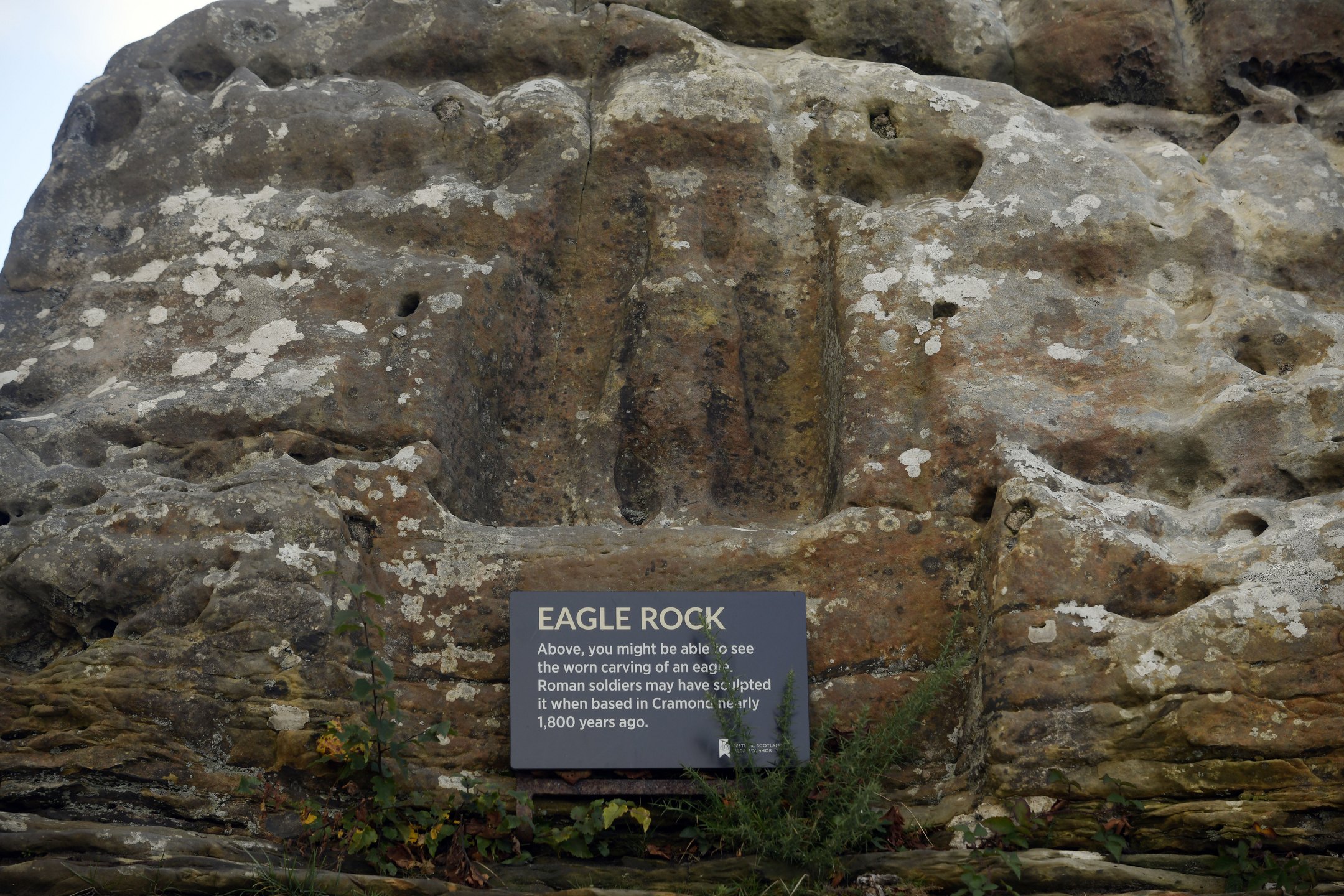 Close-up of Eagle Rock showing a worn vertical carving on the stone face with an information sign mounted below.