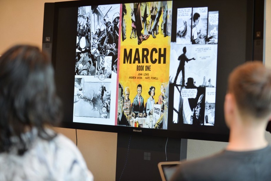 Image taken over the shoulders of two participants of the HES arts Awards showing a screen that reads "March - Book One".