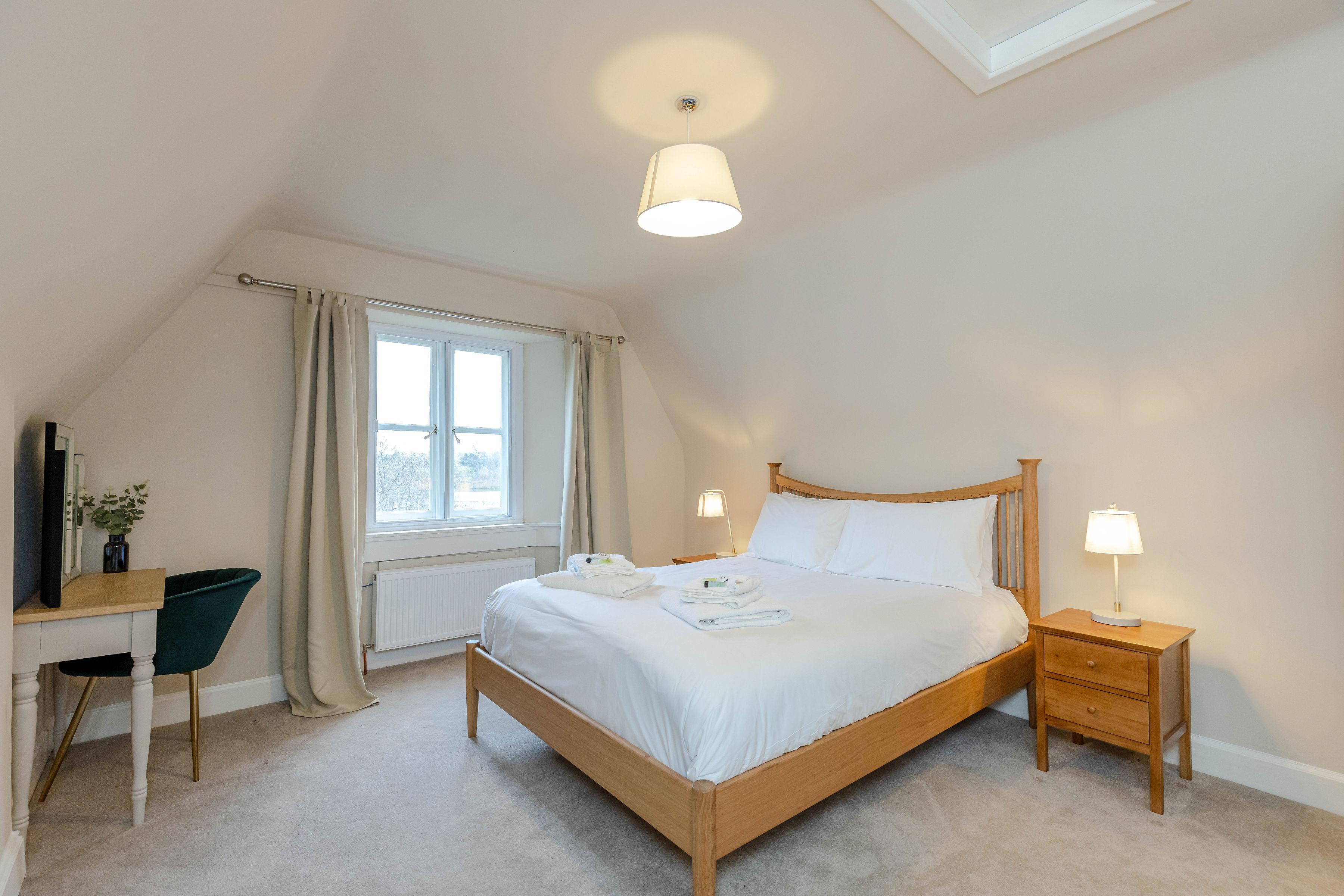 A cream-coloured bedroom with a wooden double bed and white sheets, with towels and bath products set out on the bed