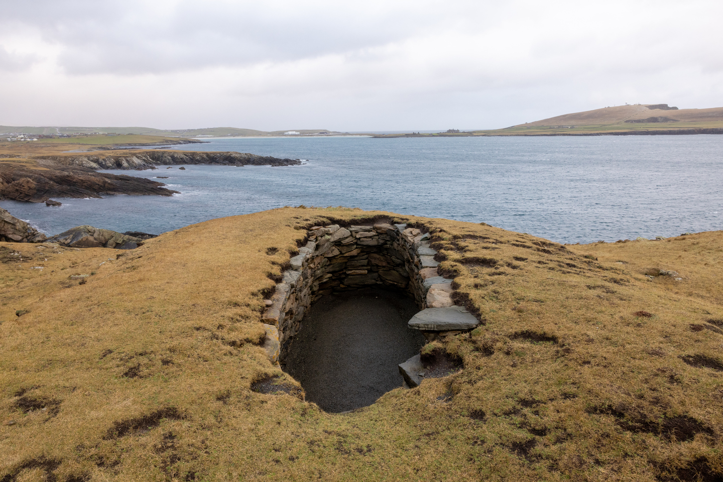 Part of a stone built passage in the ground, sea is in the background.