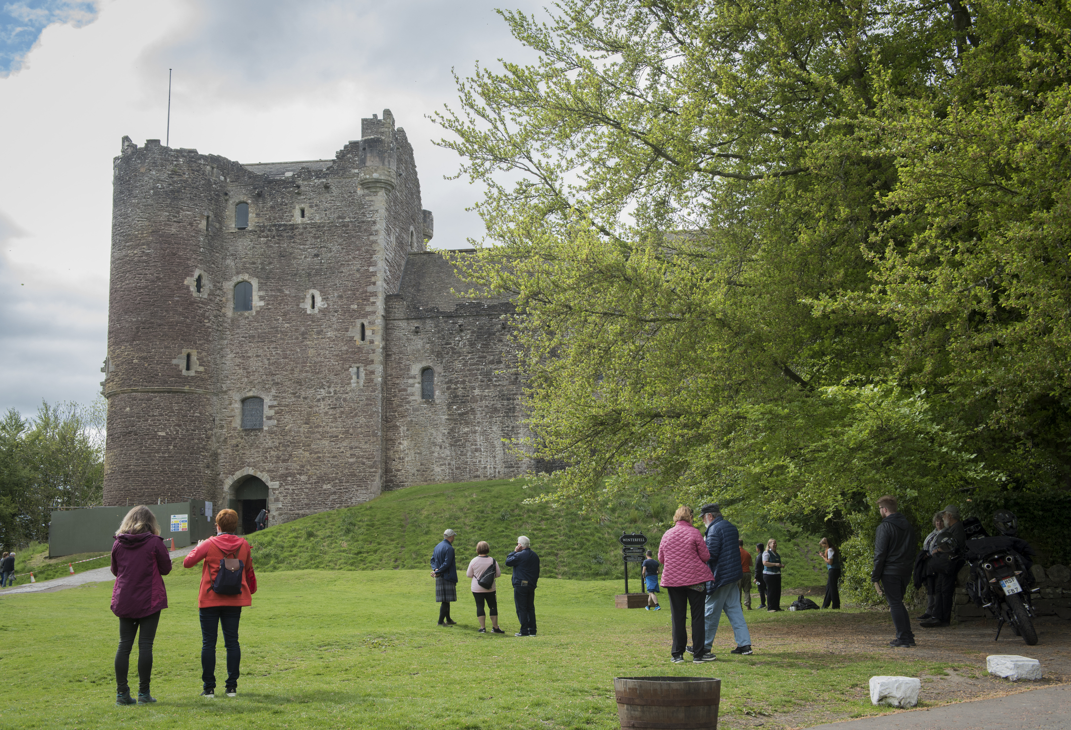 Visitors mill around in a grassy area in front the imposing ruin of a stone castle.