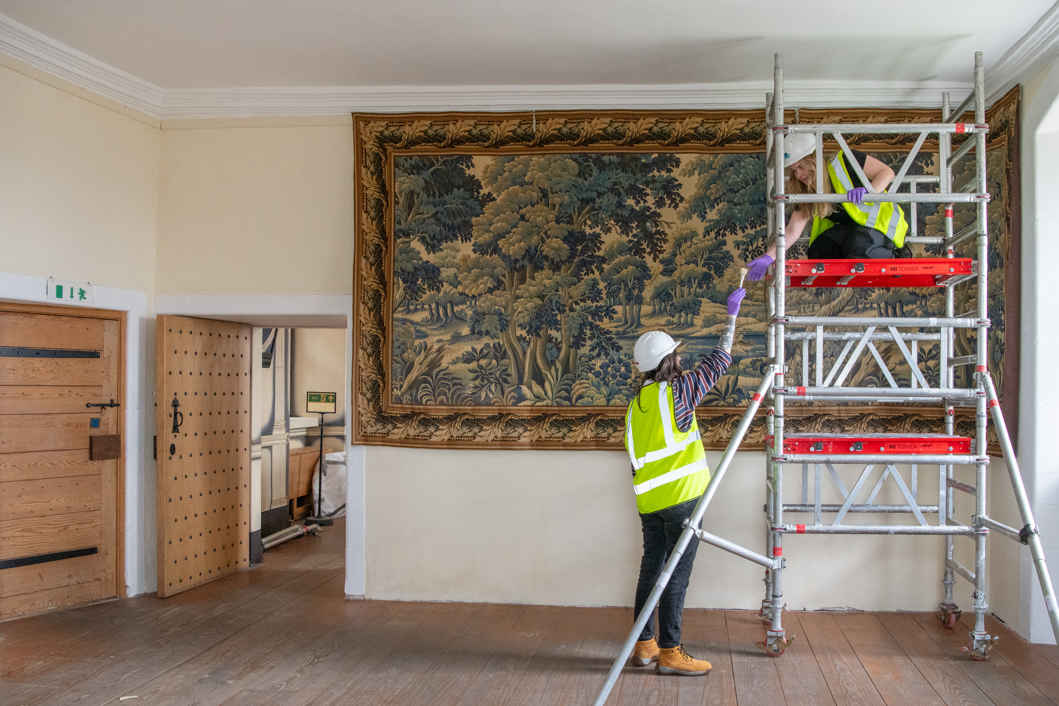 Members of the Historic Environment Scotland Collections team use a small scaffold to access hard to reach parts of a large tapestry 
